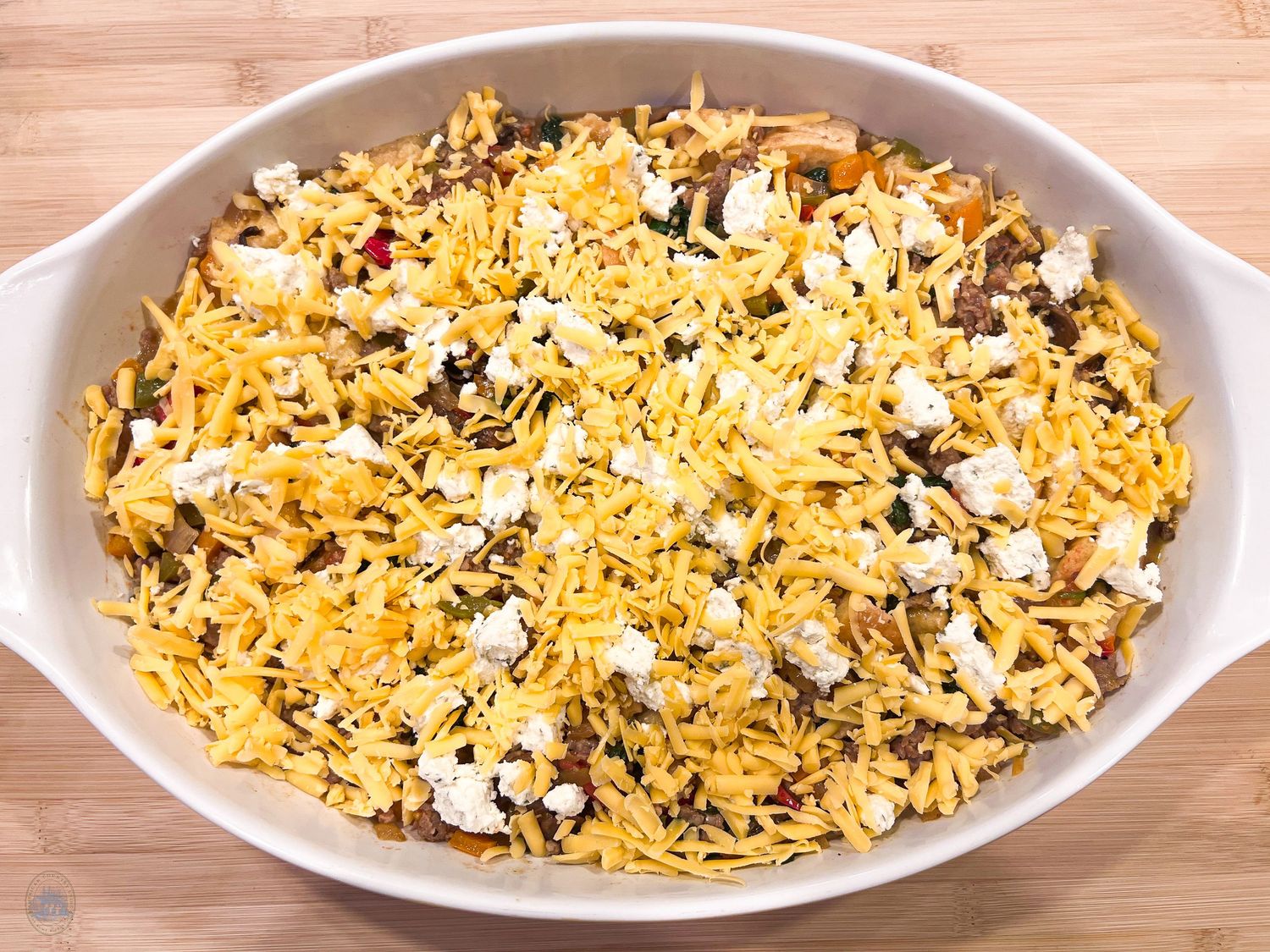 Yellow rice casserole topped with melted cheese and vegetables in oval serving dish.