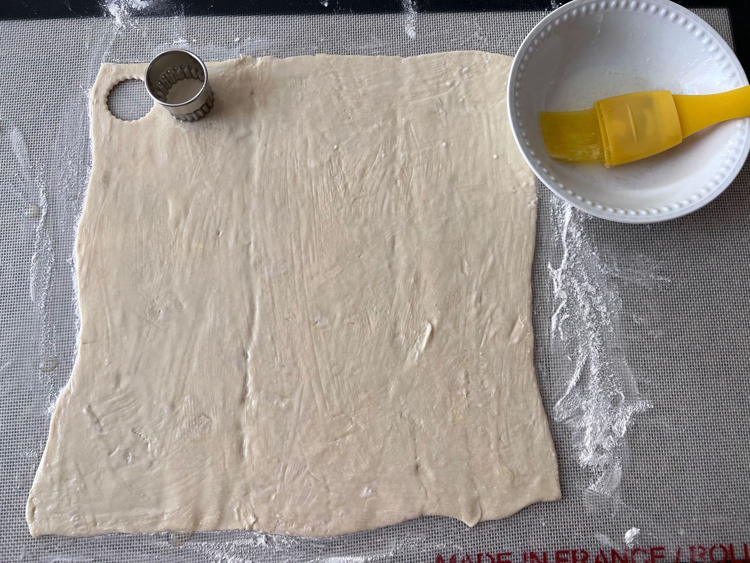 Raw pastry dough rolled out on floured surface with butter and cutter tools.
