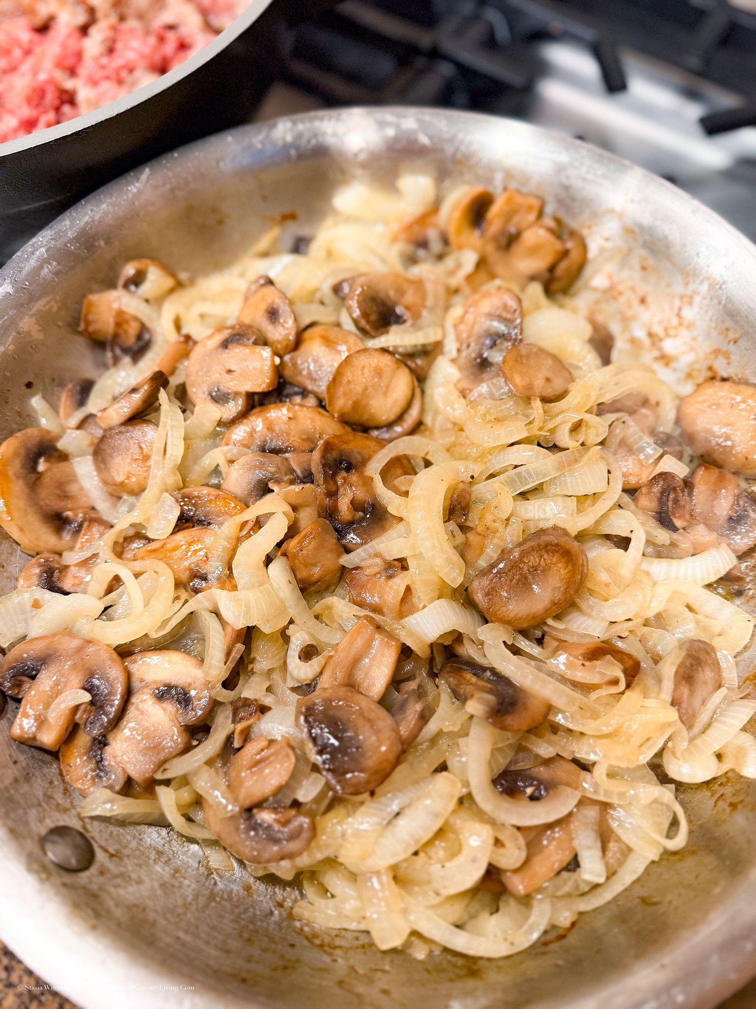 Sautéed mushrooms and caramelized onions cooking in a stainless steel skillet on a stovetop.