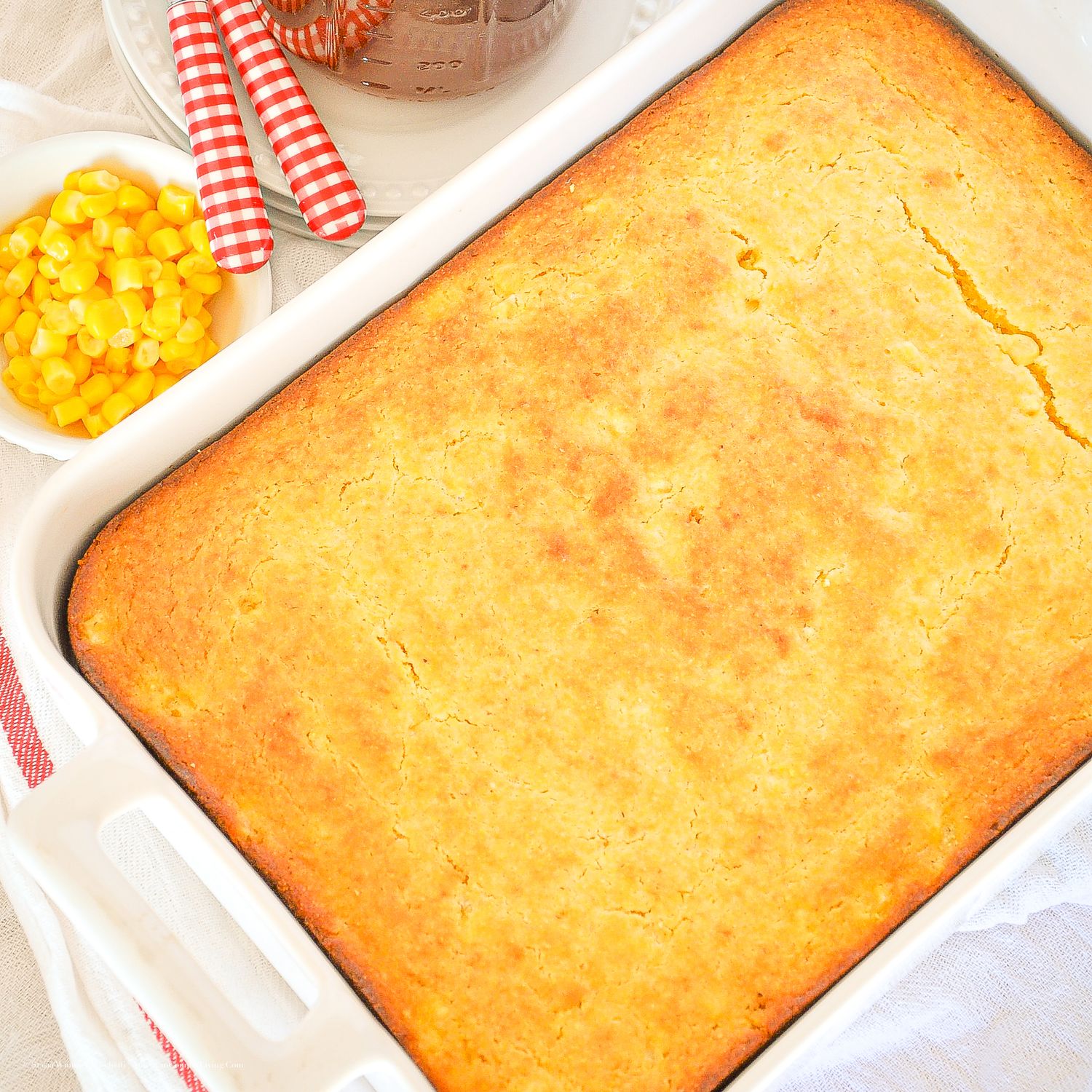 Golden cornbread baked in a white casserole dish, served with a side of sweet corn kernels.