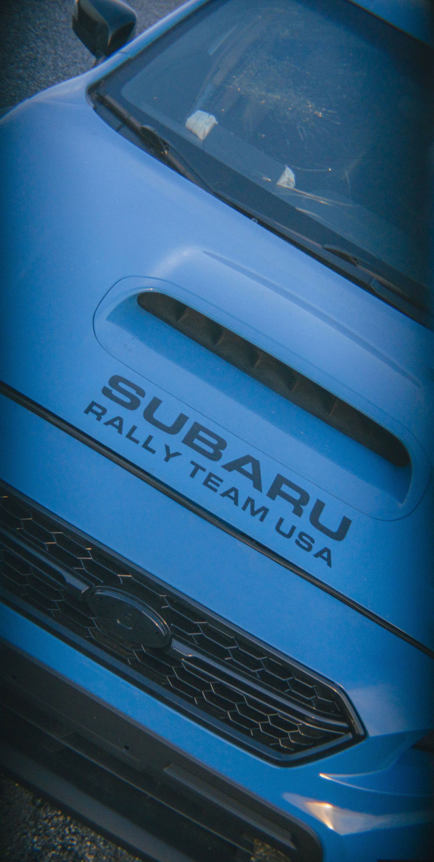 Hood shot of a hyper blue Subaru STI with a vinyl that says 