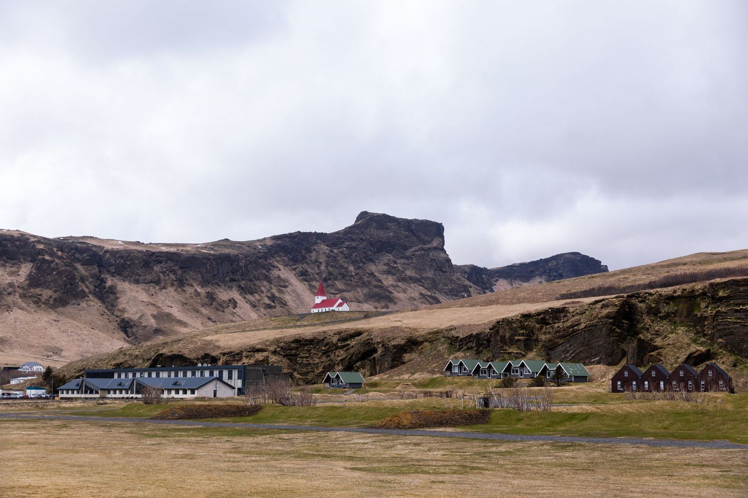 Small village with colorful buildings beneath dramatic cliffs in the Icelandic countryside.