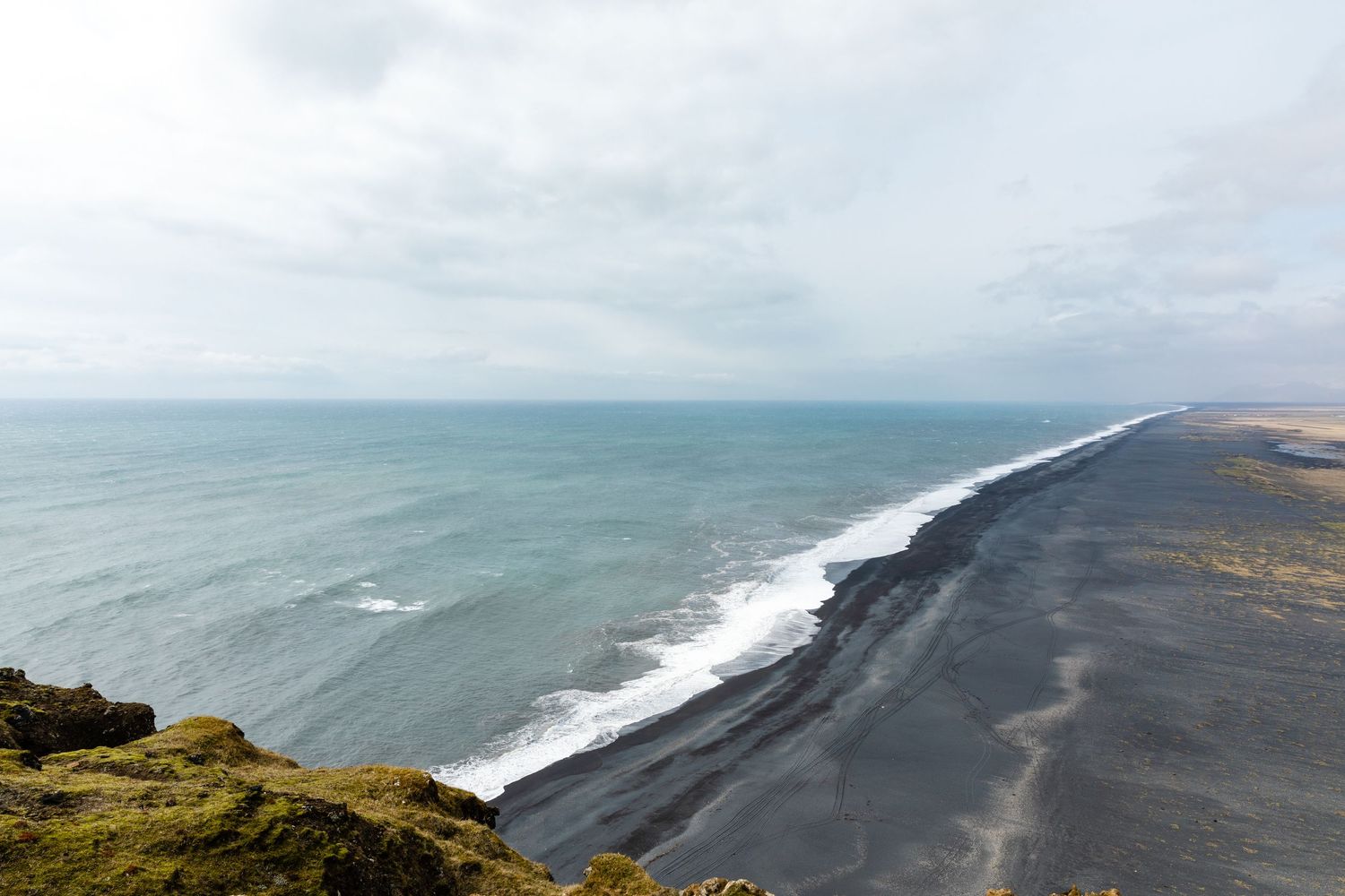 Dramatic coastline view of black sand beach meeting turquoise ocean waters in Iceland.