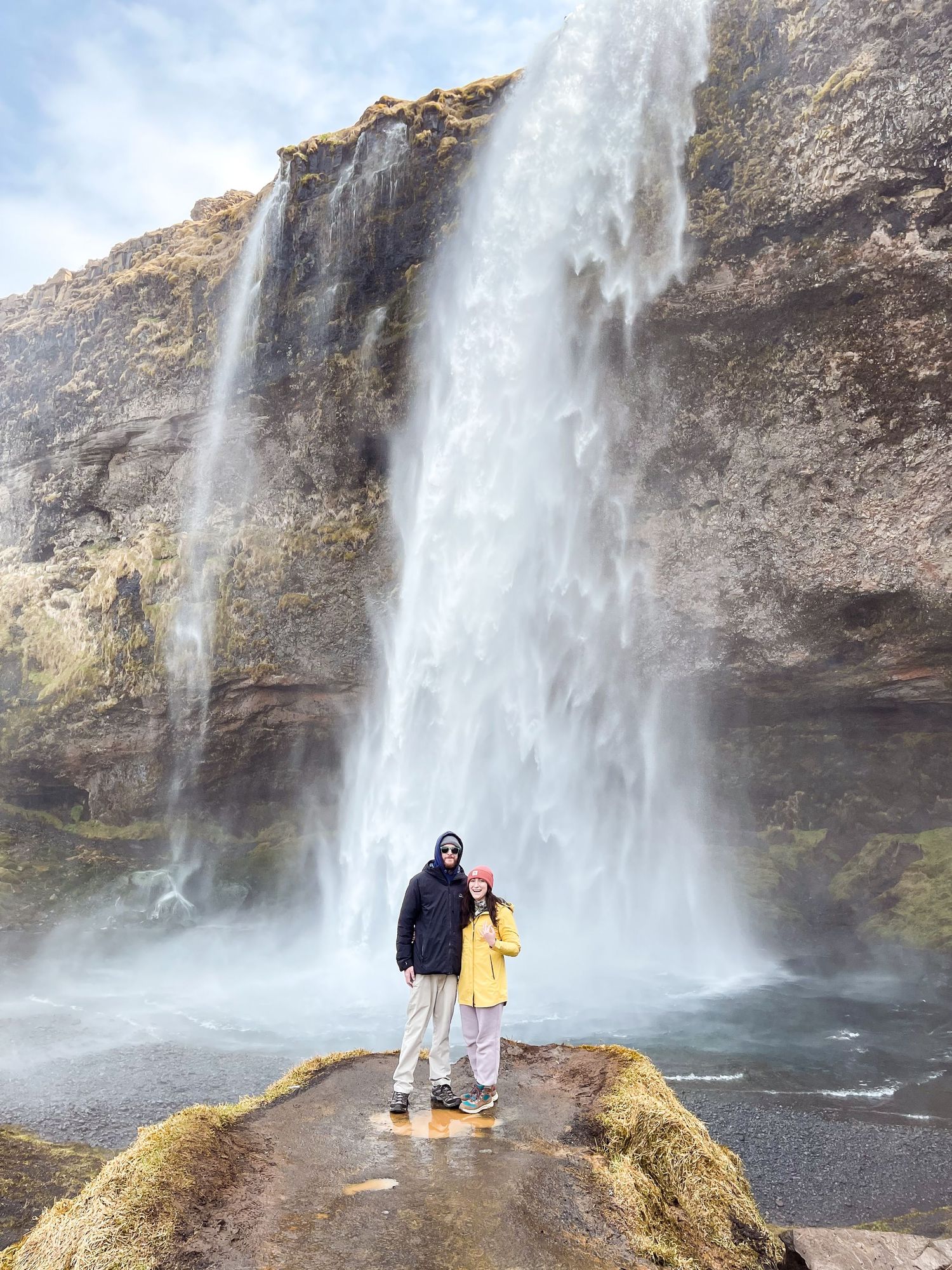 Visitors standing beneath a majestic tall waterfall in Iceland's rugged landscape.