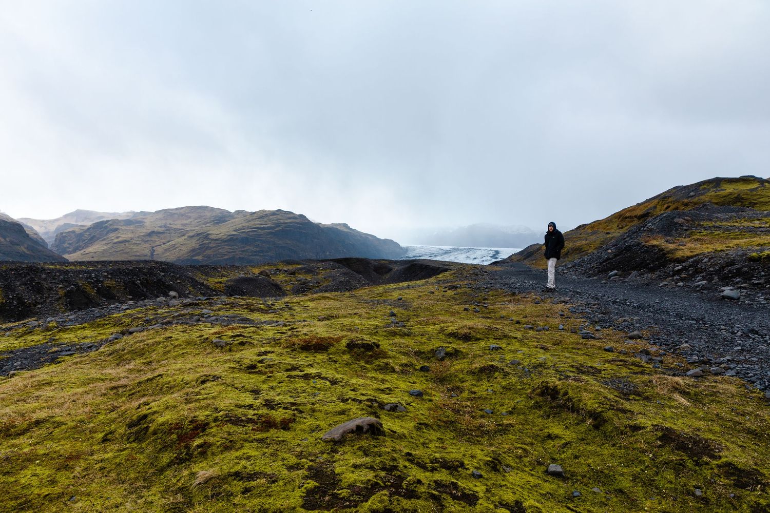 Hiker on moss-covered volcanic terrain with mountain views in Iceland's wilderness.