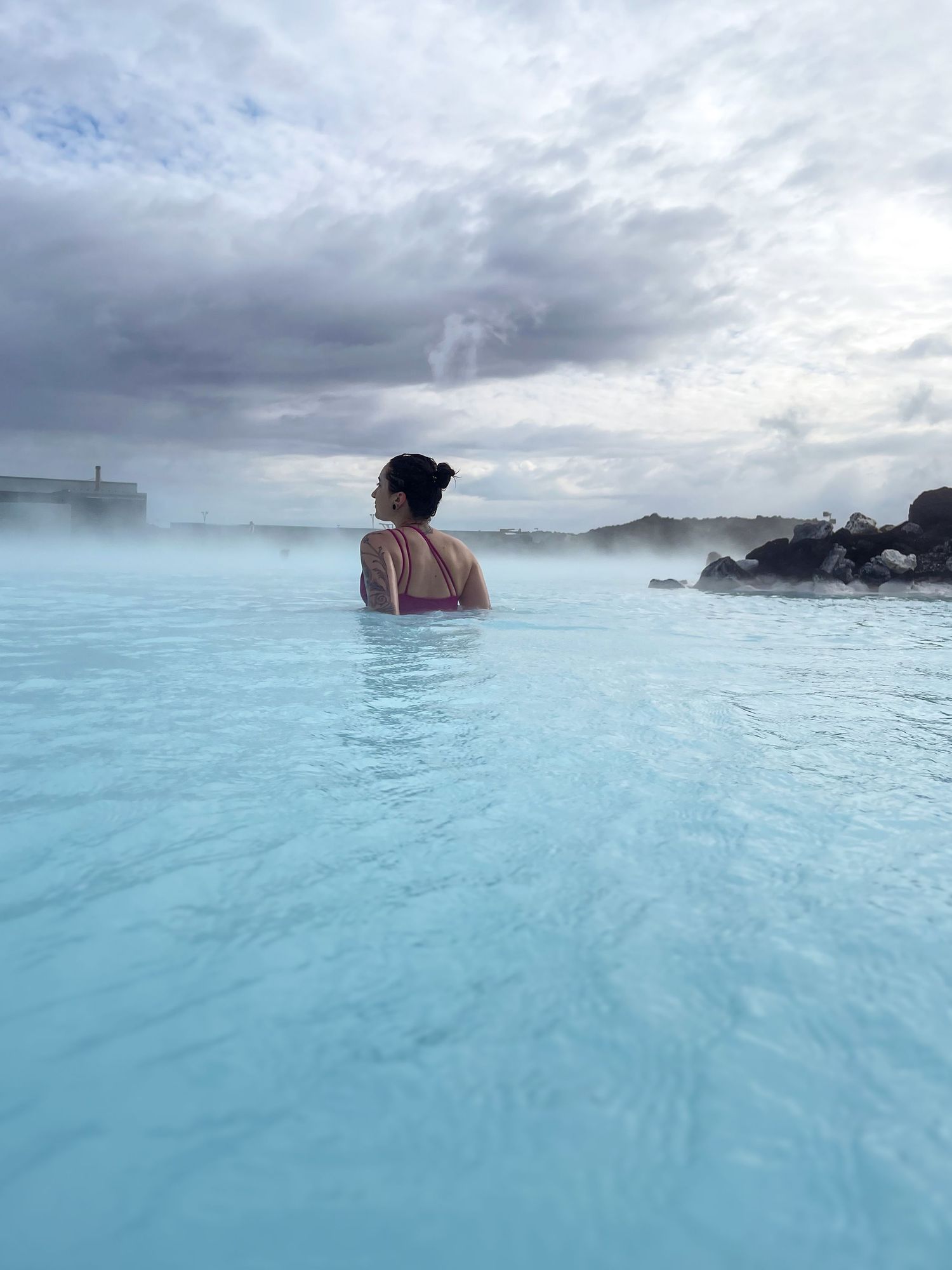 Person enjoying the milky blue waters of Iceland's Blue Lagoon geothermal spa on a cloudy day.