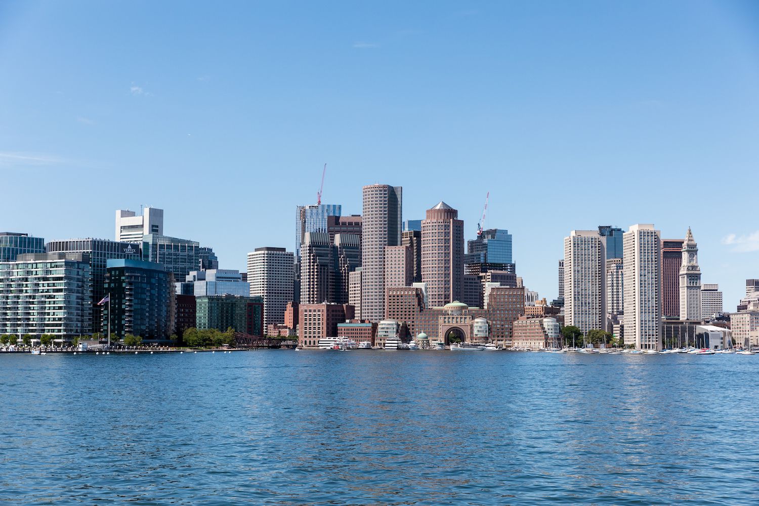 Boston skyline view from harbor showing modern office buildings and waterfront on sunny day.