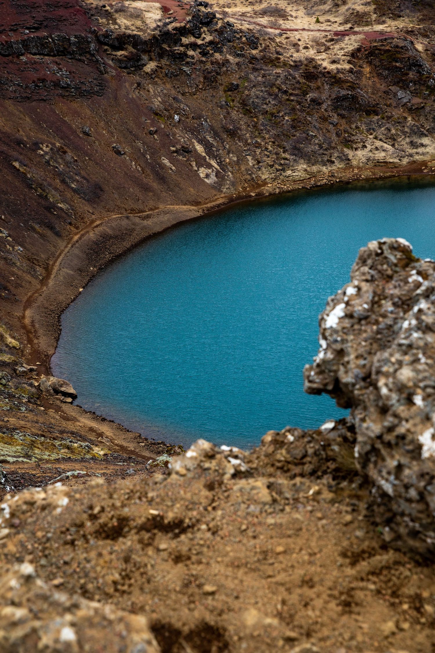 Stunning turquoise blue crater lake surrounded by volcanic rocks and rugged terrain.