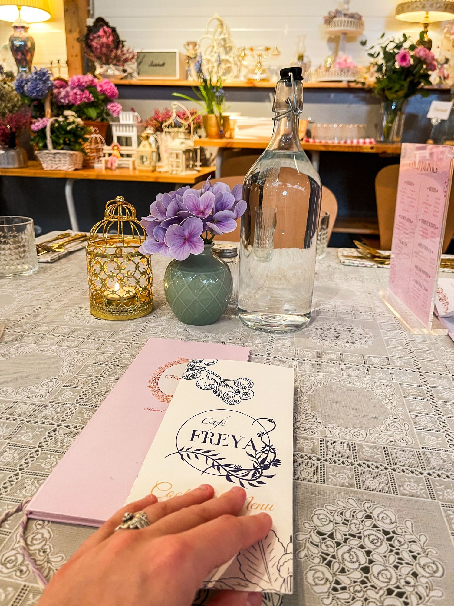 Table setting with pink notebook, purple flowers, and glass bottle in cozy interior.