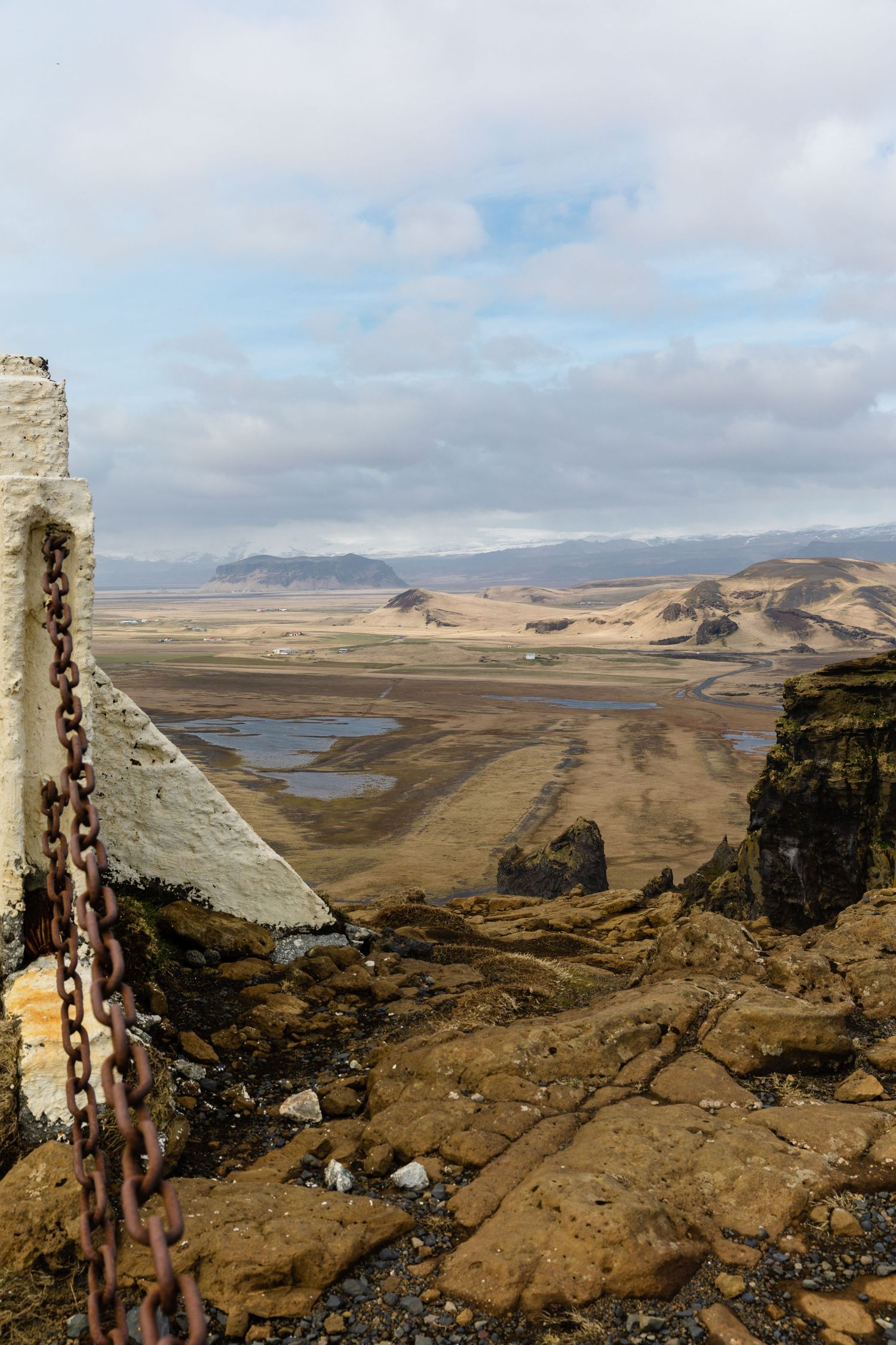 Ancient rock formations and chains overlook a vast Icelandic valley with winding rivers.