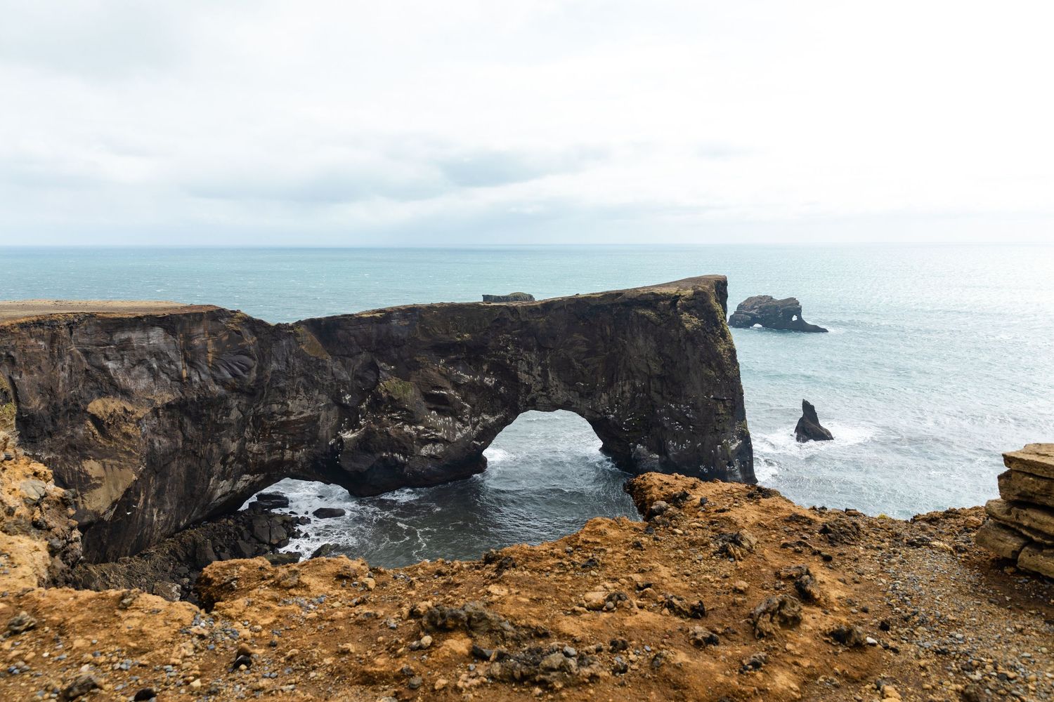 Dramatic natural stone arch formation along rocky coastline under cloudy skies.