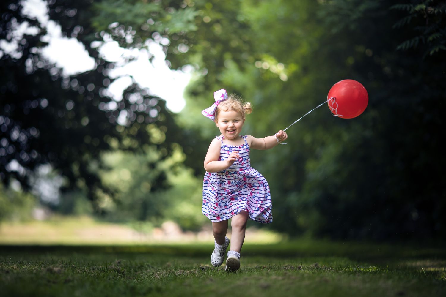 Small figure in a purple dress running with a red balloon in a park setting.