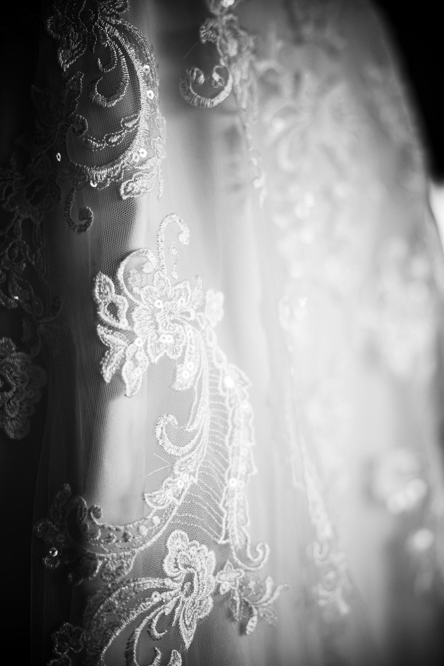 Detailed black and white macro shot of delicate lace embroidery on wedding dress fabric.