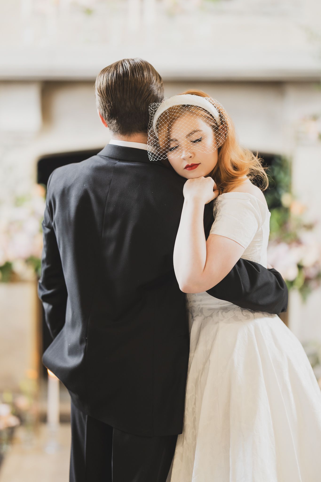 Romantic vintage wedding couple embrace in intimate moment before decorated fireplace.