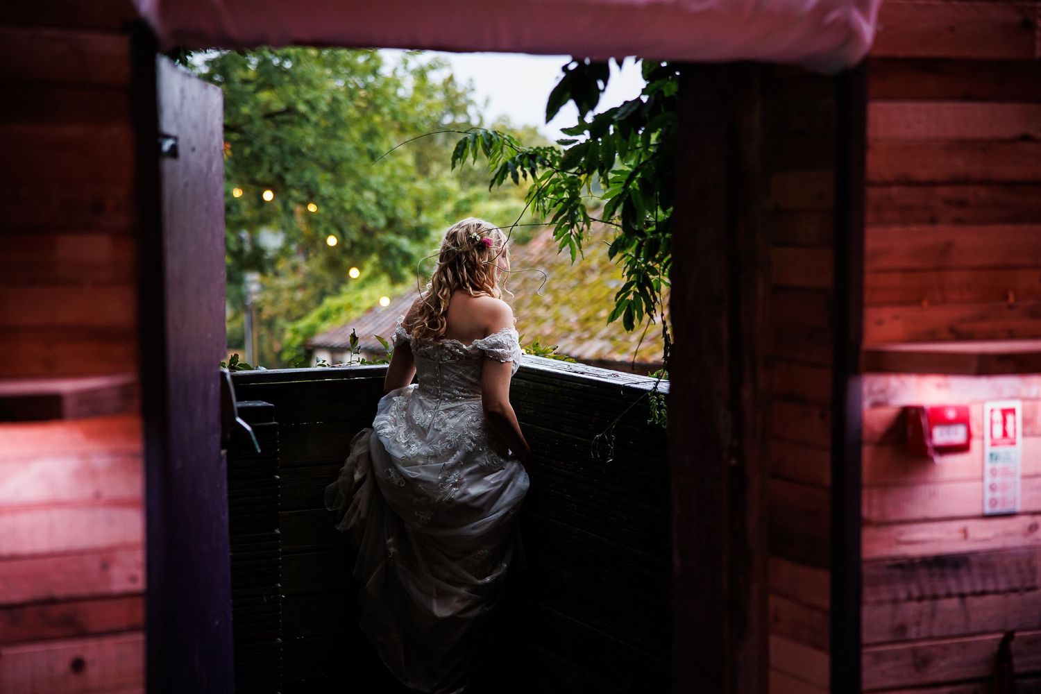 Woman in formal dress looking out from a rustic wooden building interior.