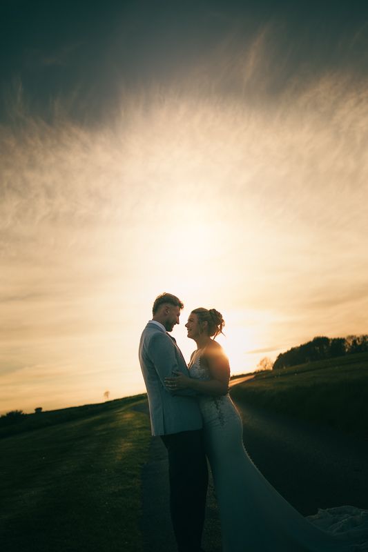 A couple embraces in silhouette against a stunning golden sunset sky on their wedding day outdoors.
