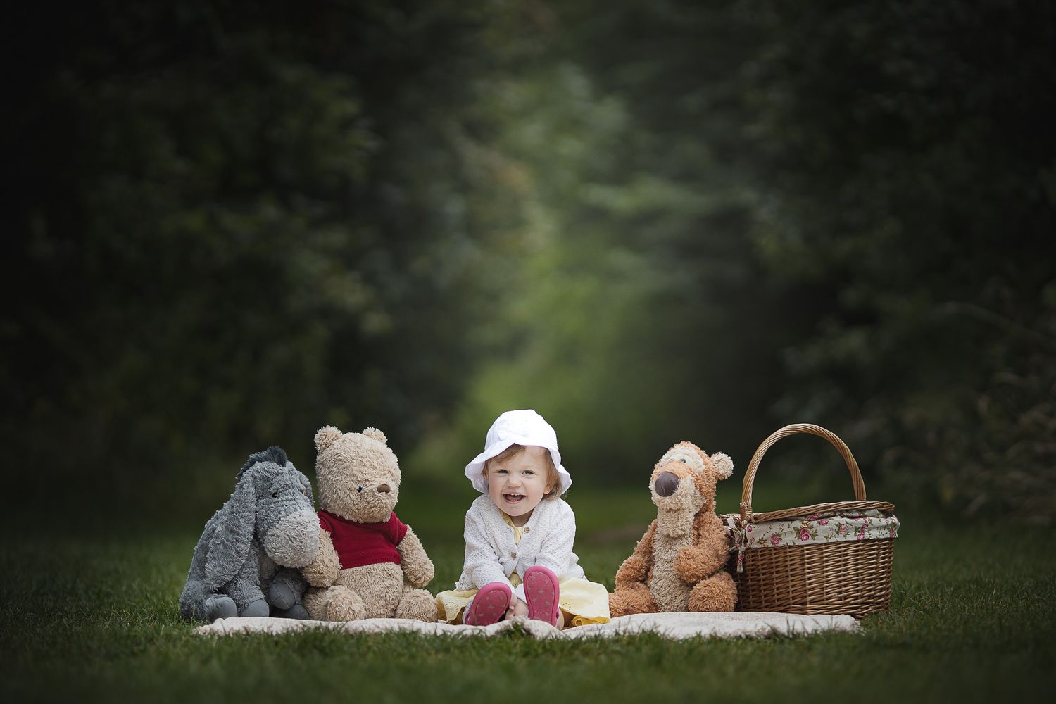 A picnic scene with stuffed teddy bears and a wicker basket on a green lawn.