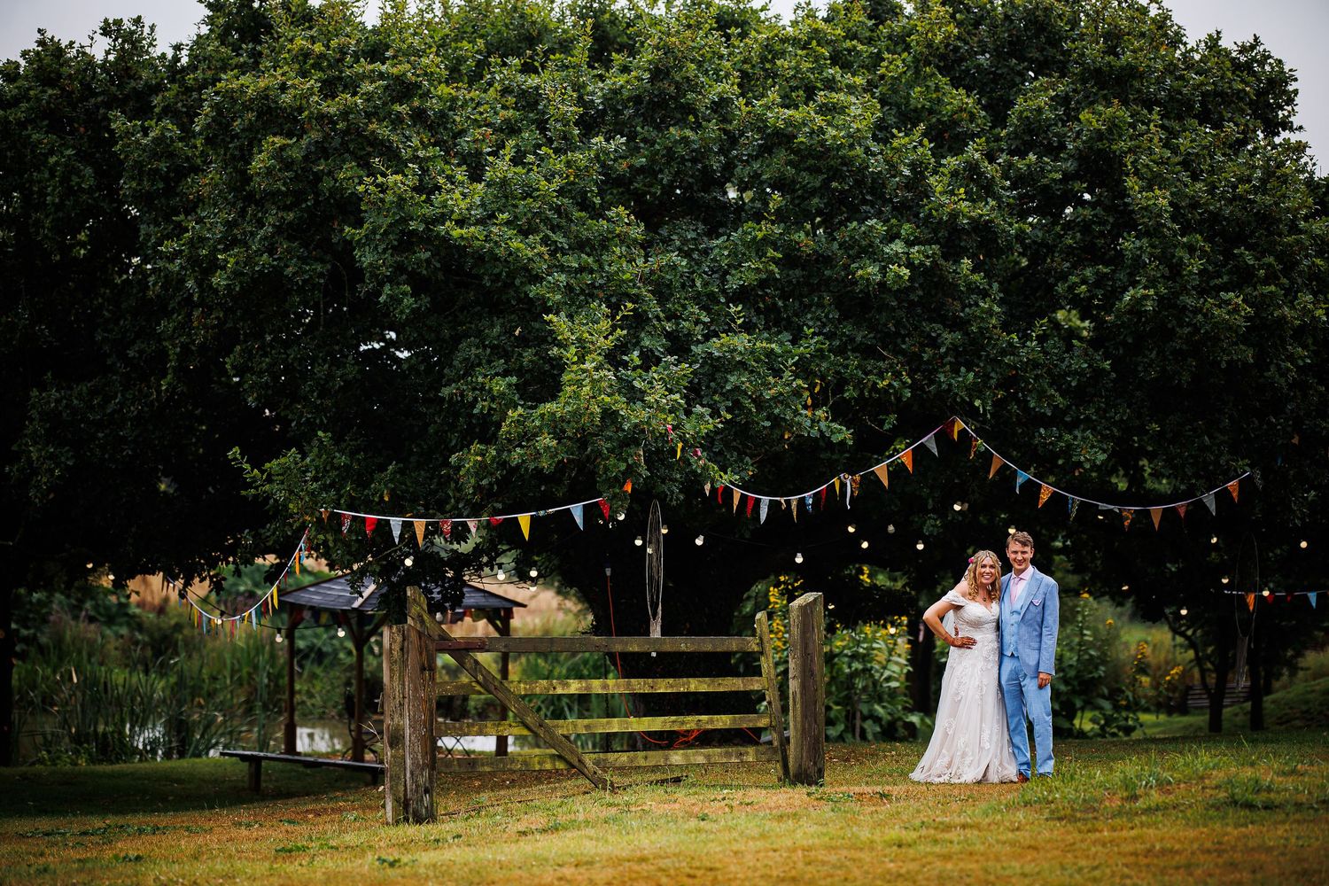 String lights hang over a rustic garden fence as a couple celebrates their wedding day.
