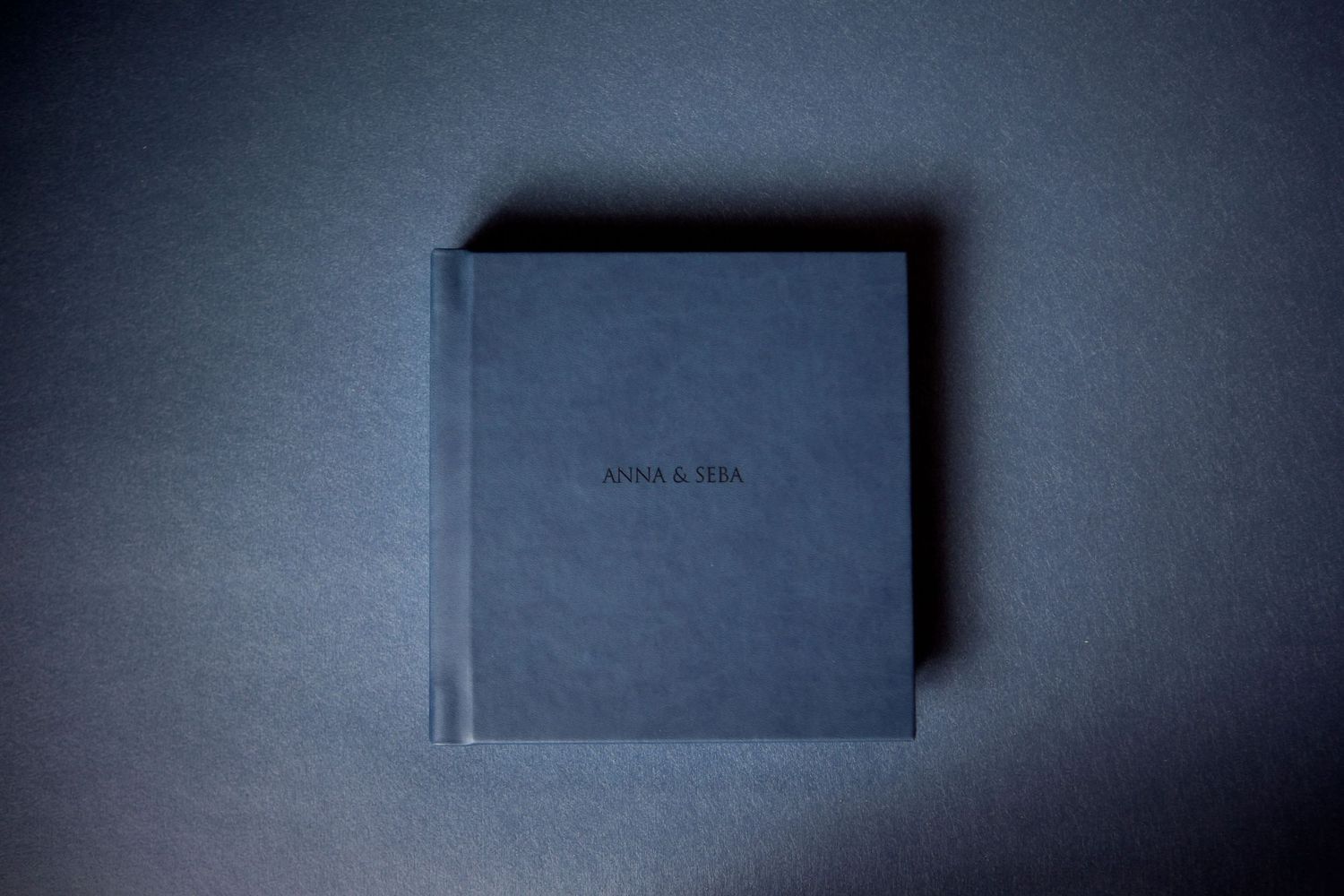 A minimalist dark gray hardcover book photographed on a plain surface with dramatic moody lighting.