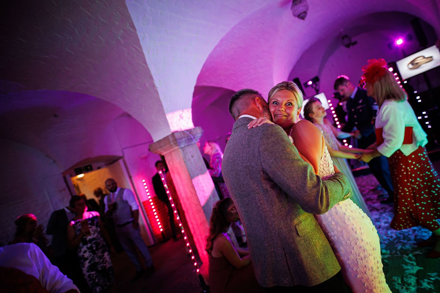 Couples dancing in a dimly lit venue with purple ambient lighting at a wedding reception.