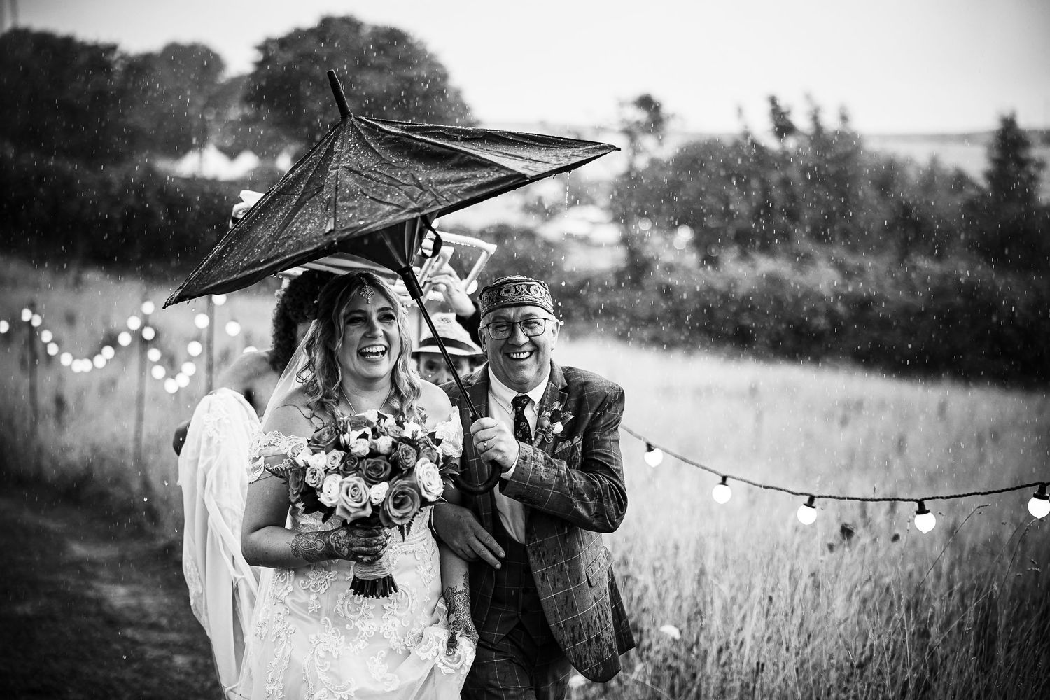 A couple struggles with an inverted umbrella on their windswept wedding day in black and white.