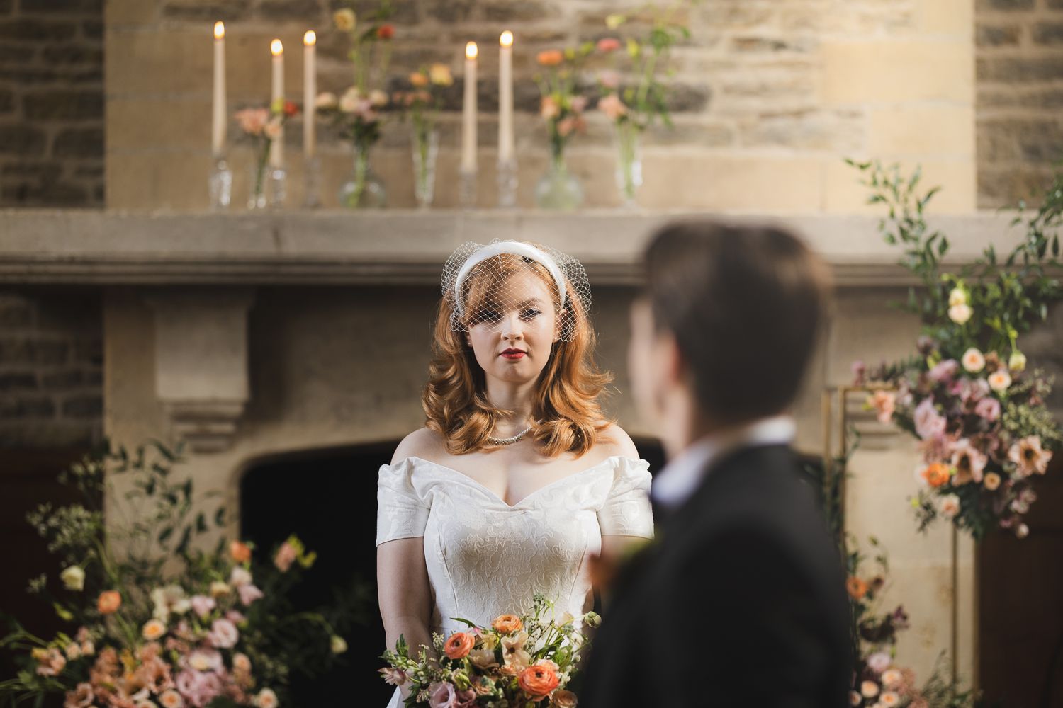 Couple exchanging vows in front of stone fireplace decorated with candles and florals.