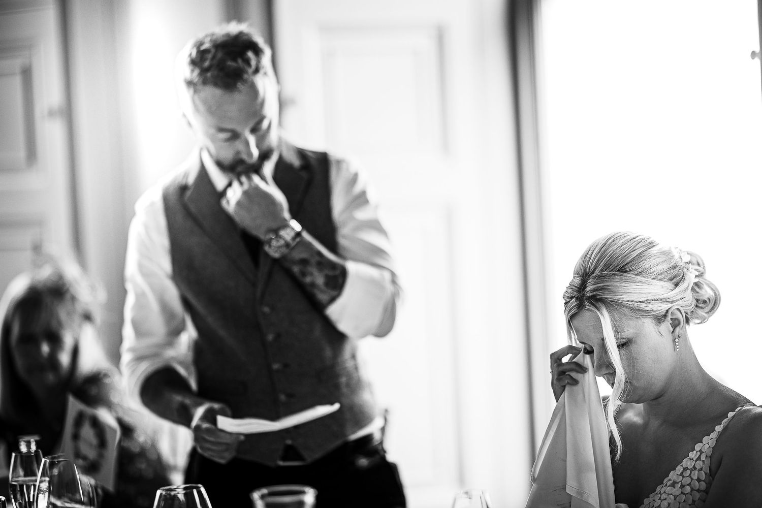 Black and white candid moment of wedding speeches in natural window light.