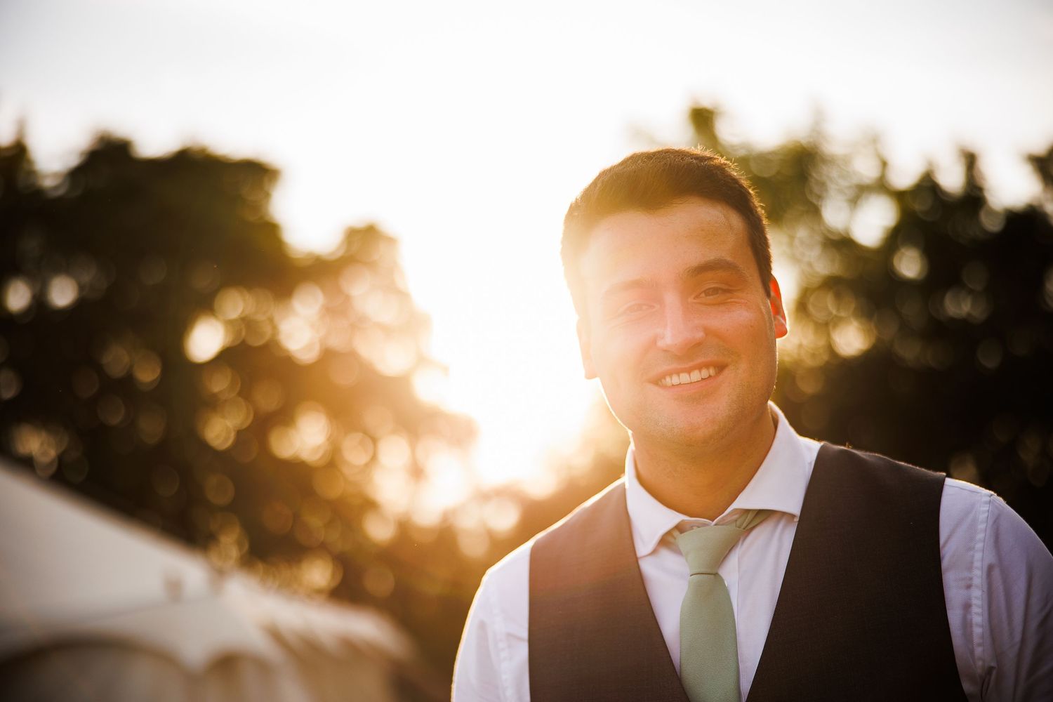 Portrait of someone wearing a vest and tie with golden sunset light glowing through trees in the background.