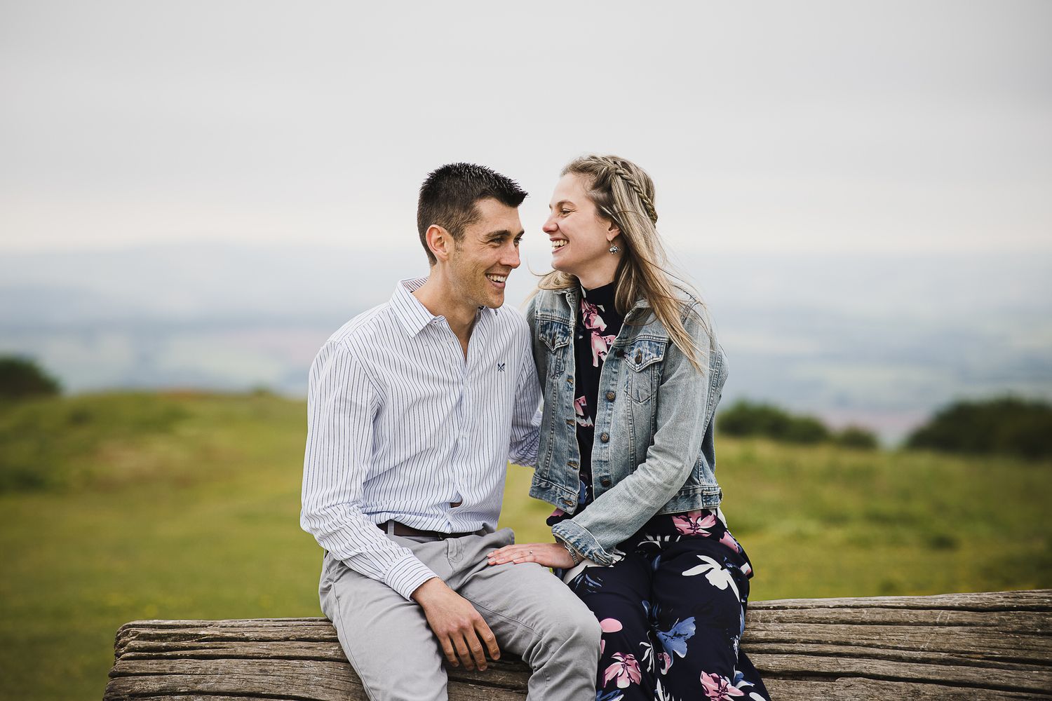 Couple sharing a laugh while sitting on wooden bench overlooking countryside.