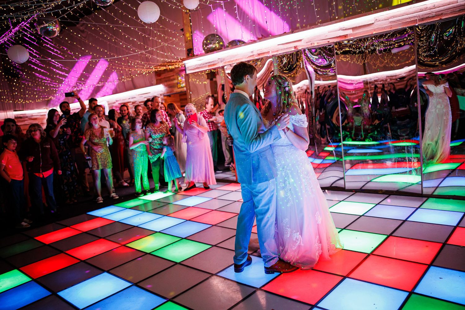 Couple dancing on illuminated multicolored dance floor at wedding reception.