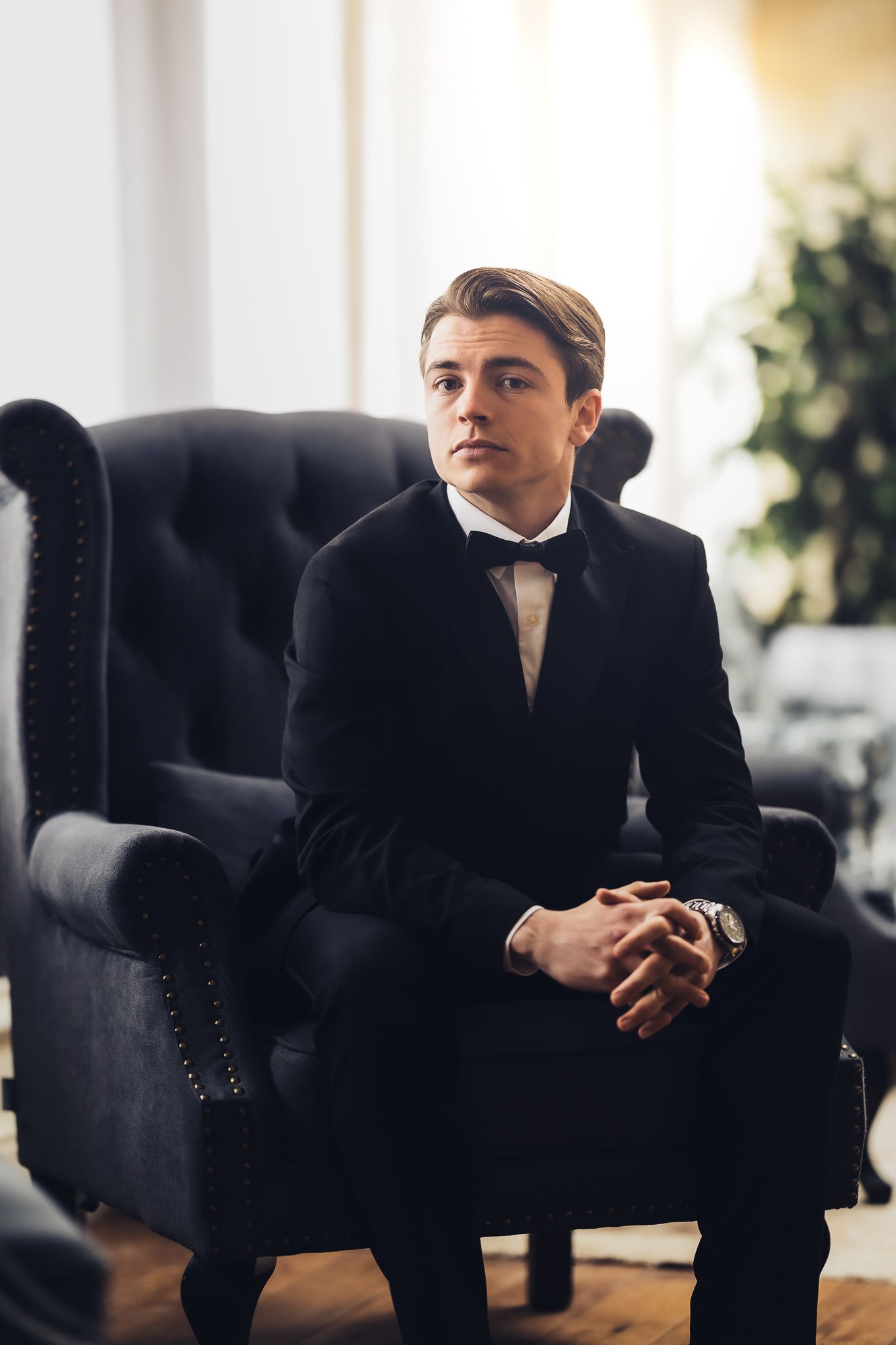 Formal portrait of a man in tuxedo seated in black armchair.