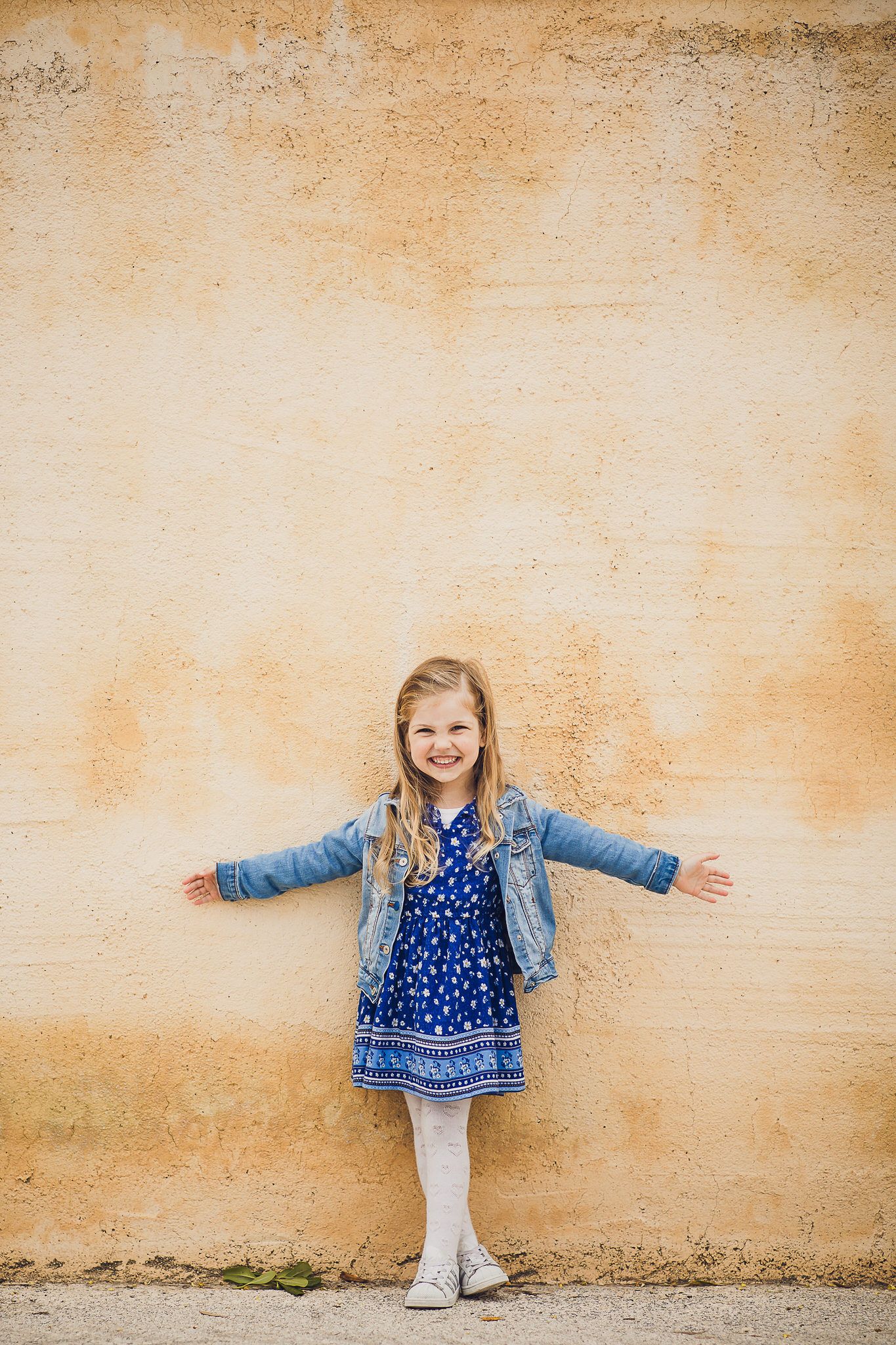Figure in a blue denim jacket and polka dot dress poses against a textured beige wall.