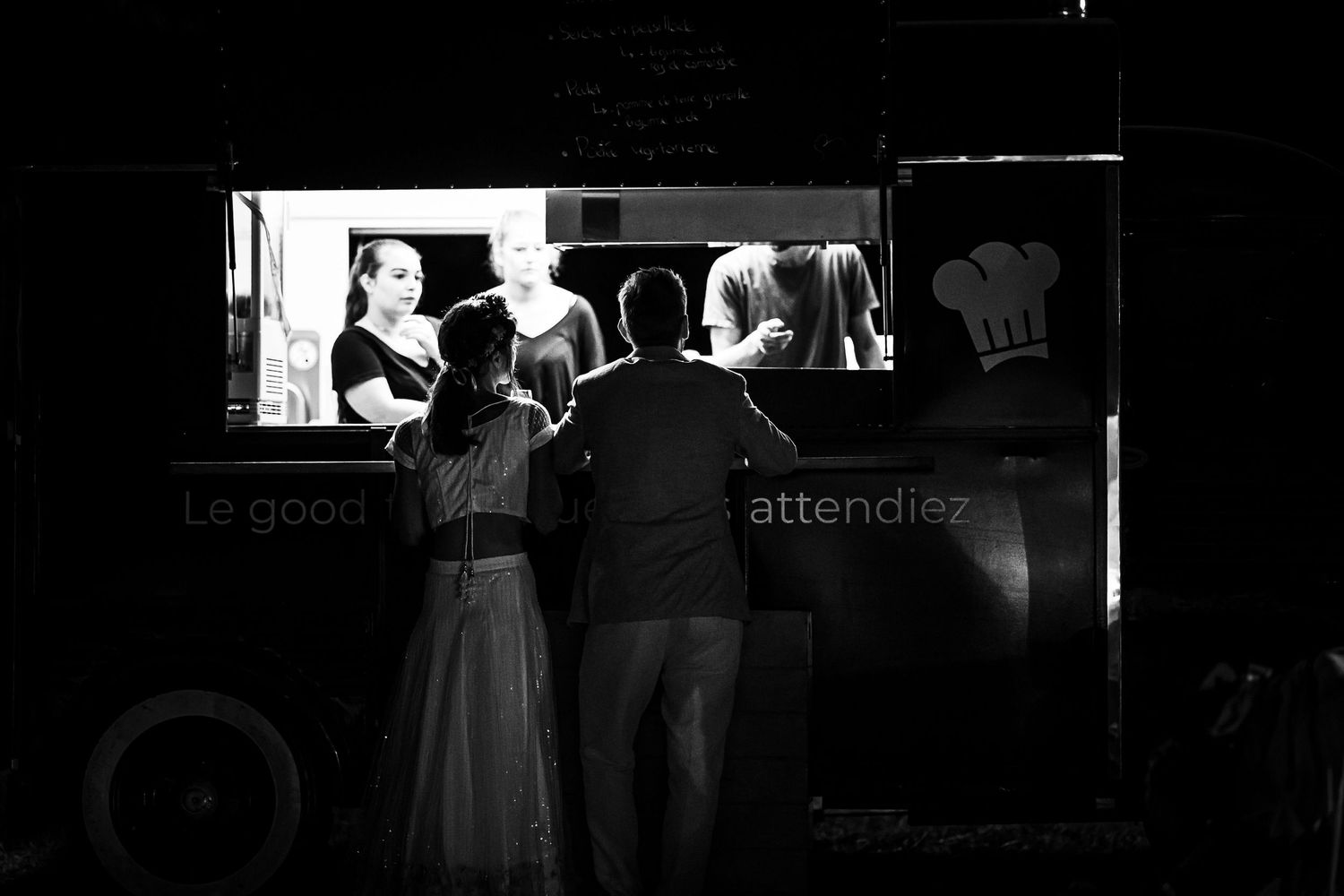A black and white image of guests ordering from a food truck at night.