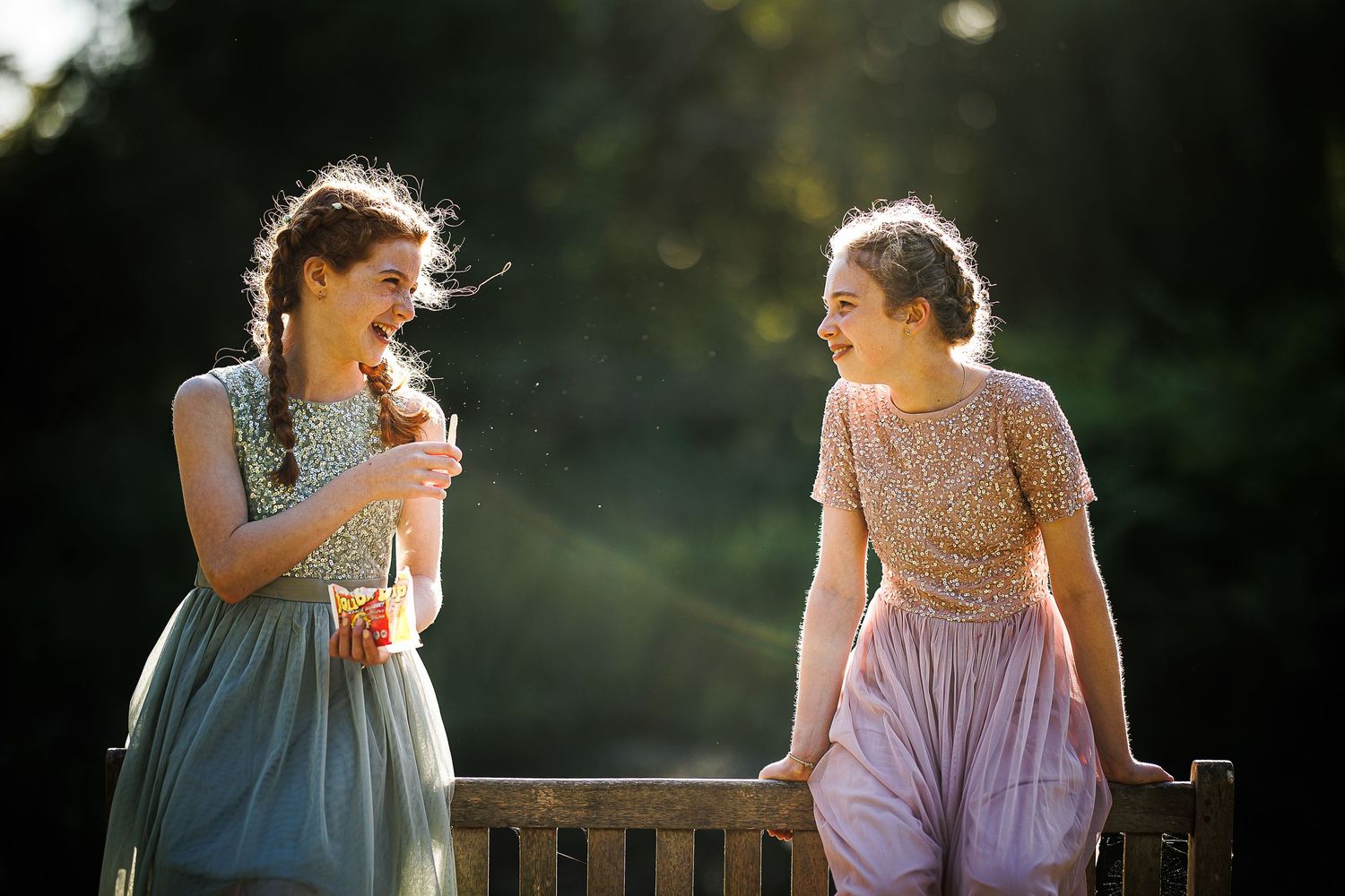Two friends share a joyful moment together on a wooden bench in golden sunlight.