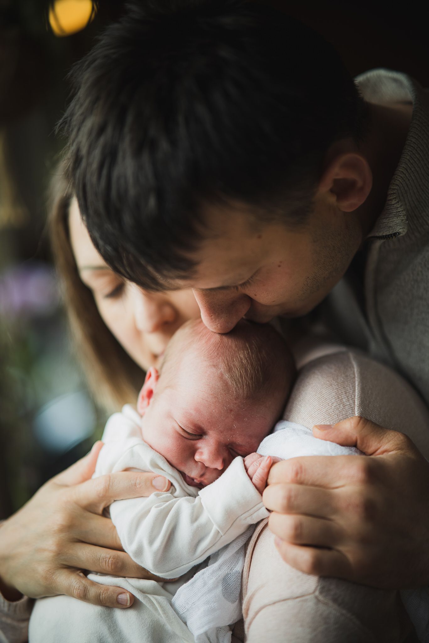 Tender moment with a newborn baby being held and kissed in soft lighting.