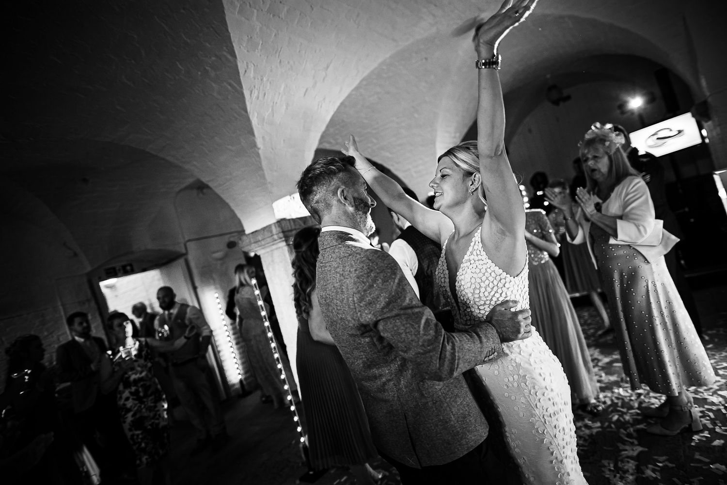 Wedding guests dancing and celebrating under arched ceilings during a lively reception.