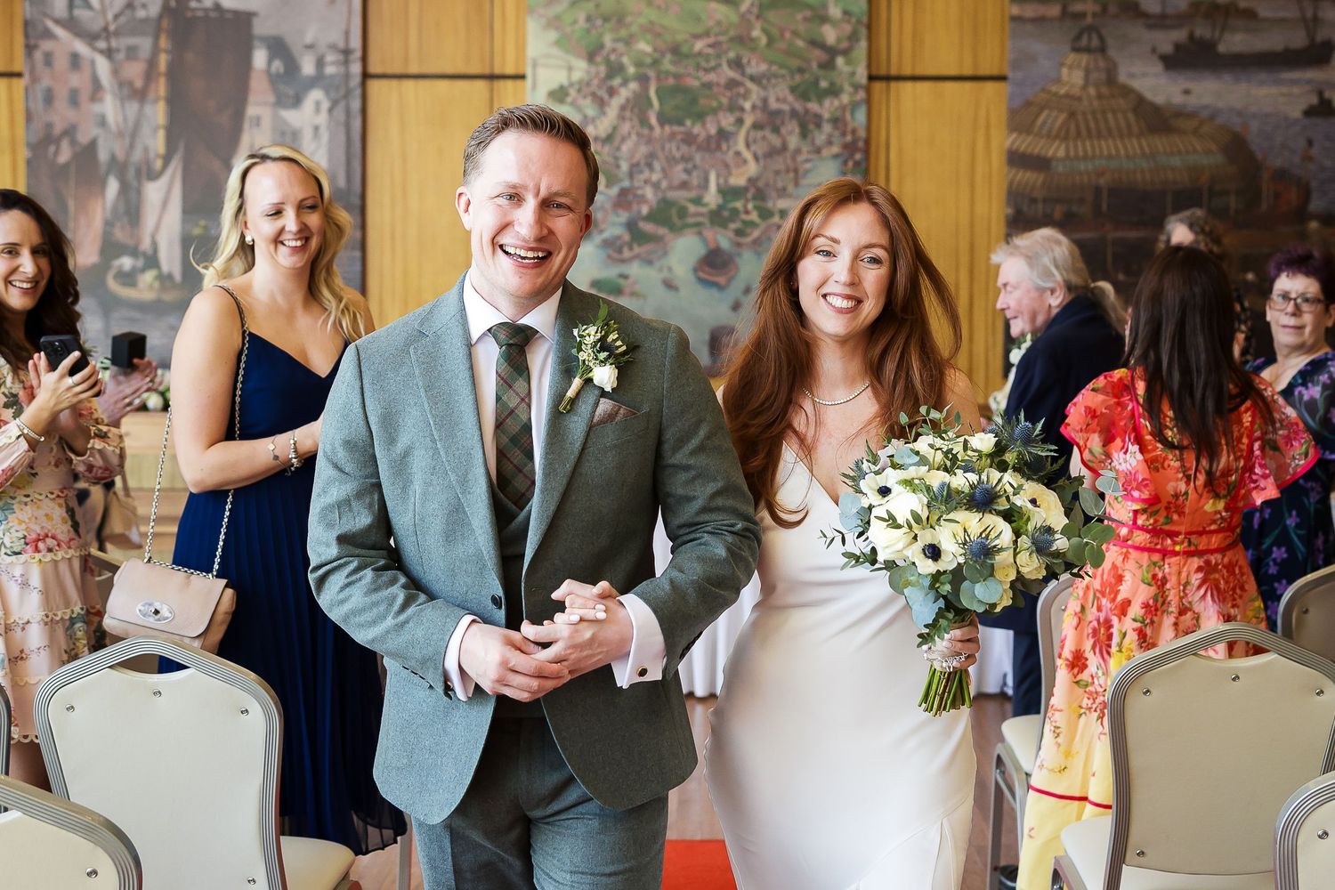 Newlyweds walking joyfully down the aisle after ceremony, bride carrying a yellow and white bouquet.