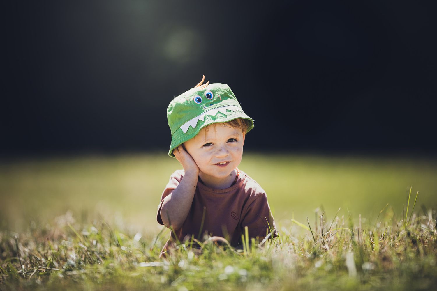 Figure wearing a green cap sits in tall grass on a sunny day.