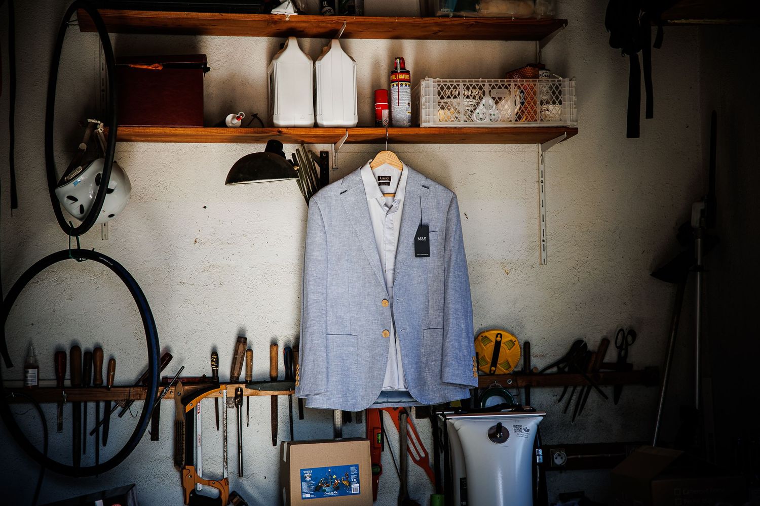 A light blue blazer hanging on a wooden shelf in a workshop or garage setting.