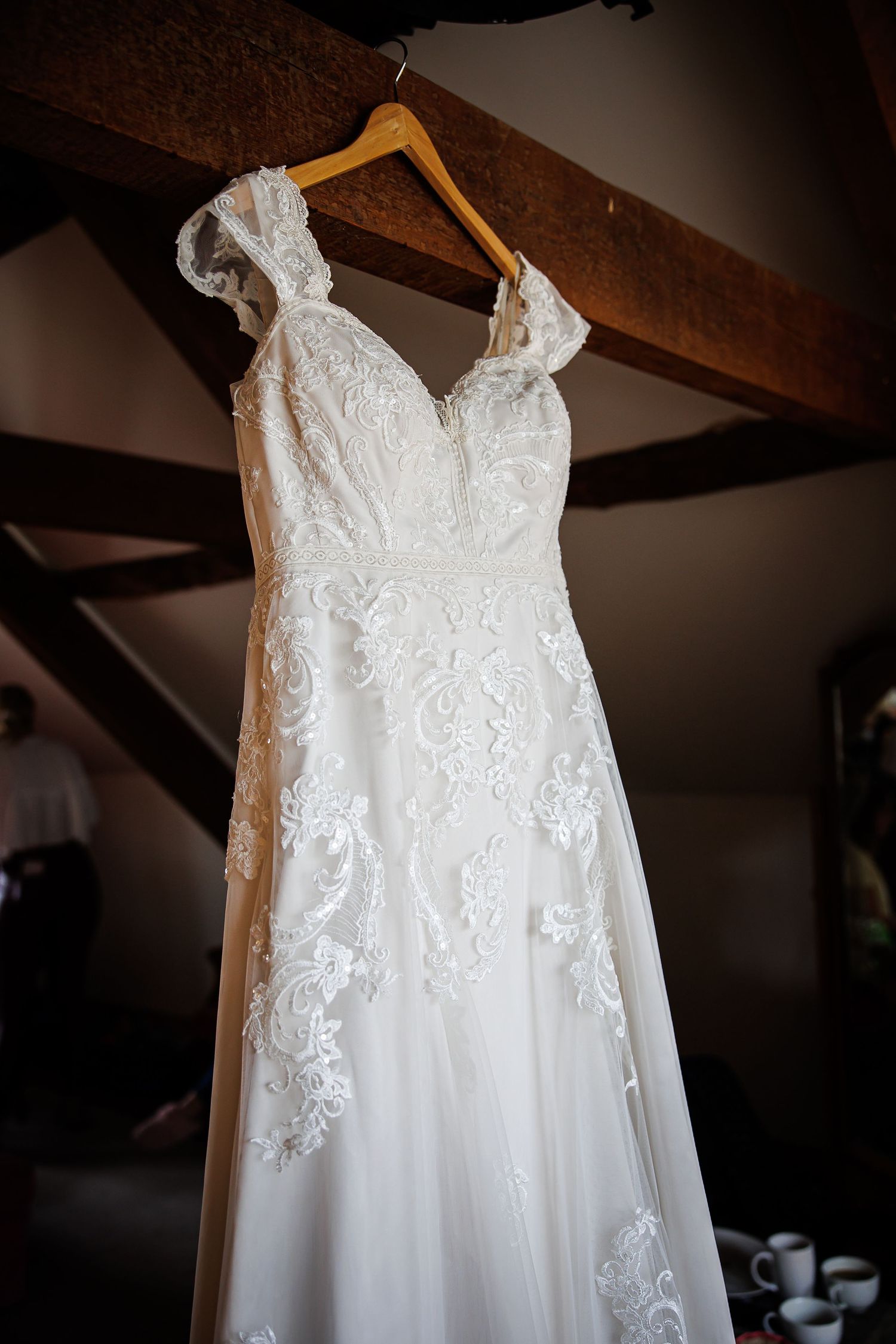 An elegant lace wedding dress with v-neck design hanging from a wooden beam.