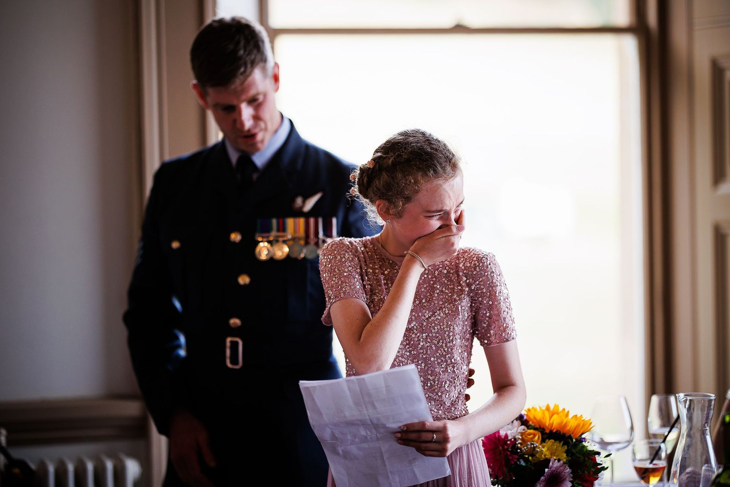 Emotional moment during wedding speech reading in sunlit room.