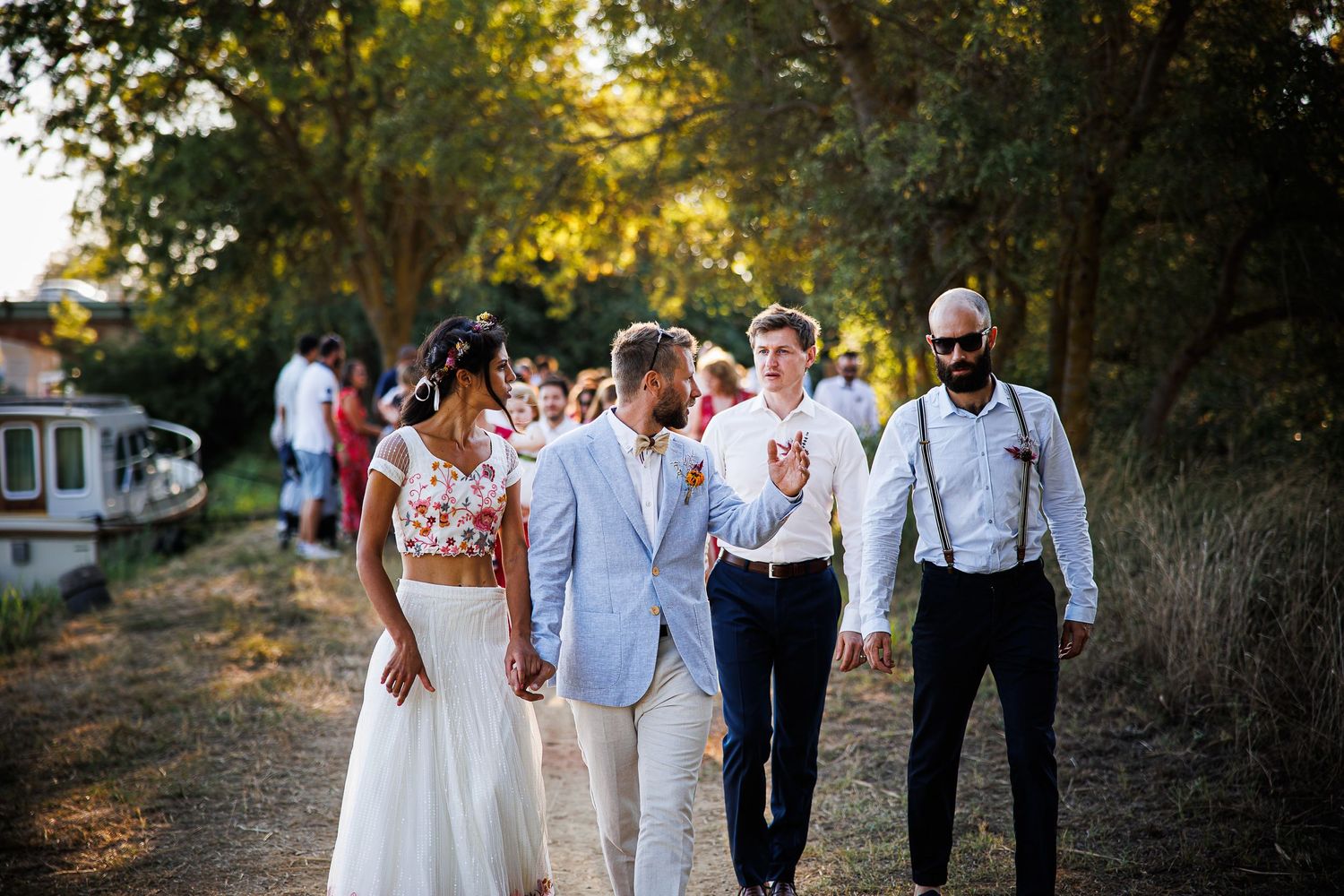 Wedding party walking together on a tree-lined path in formal attire.