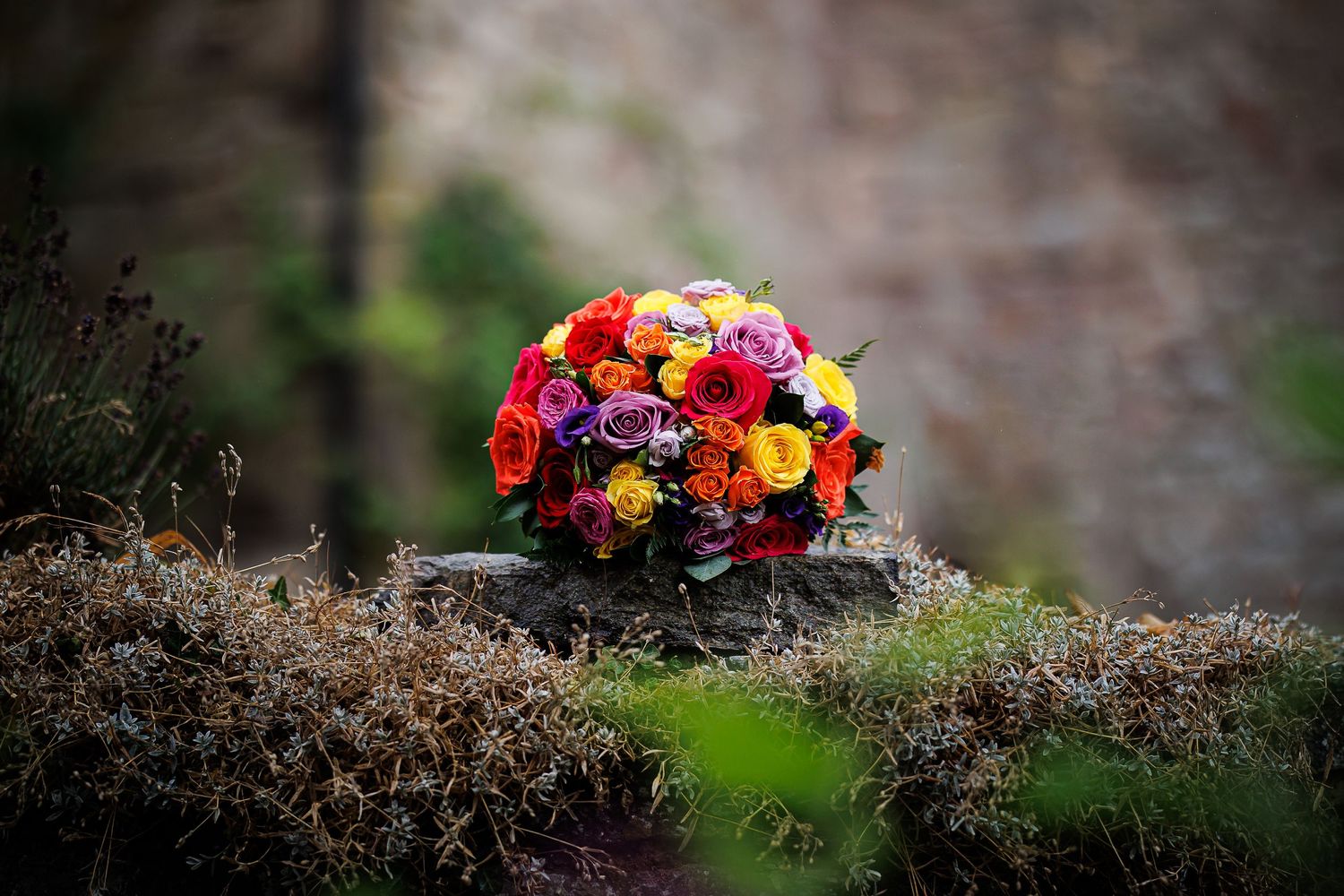 Vibrant wedding bouquet with red, purple and orange flowers rests on rustic stone.