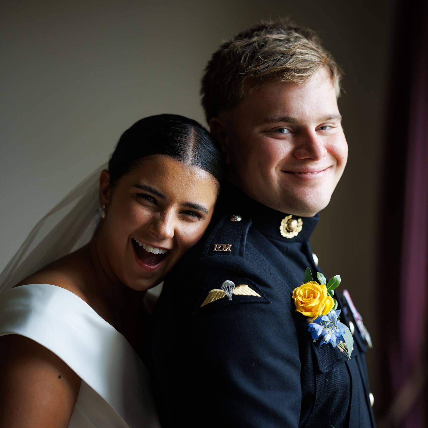 A bride in white and groom in navy dress uniform share a joyful candid moment together on their wedding day.