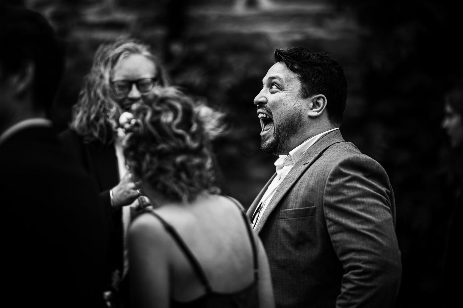 Black and white candid photo showing a person laughing joyfully at a party or celebration.