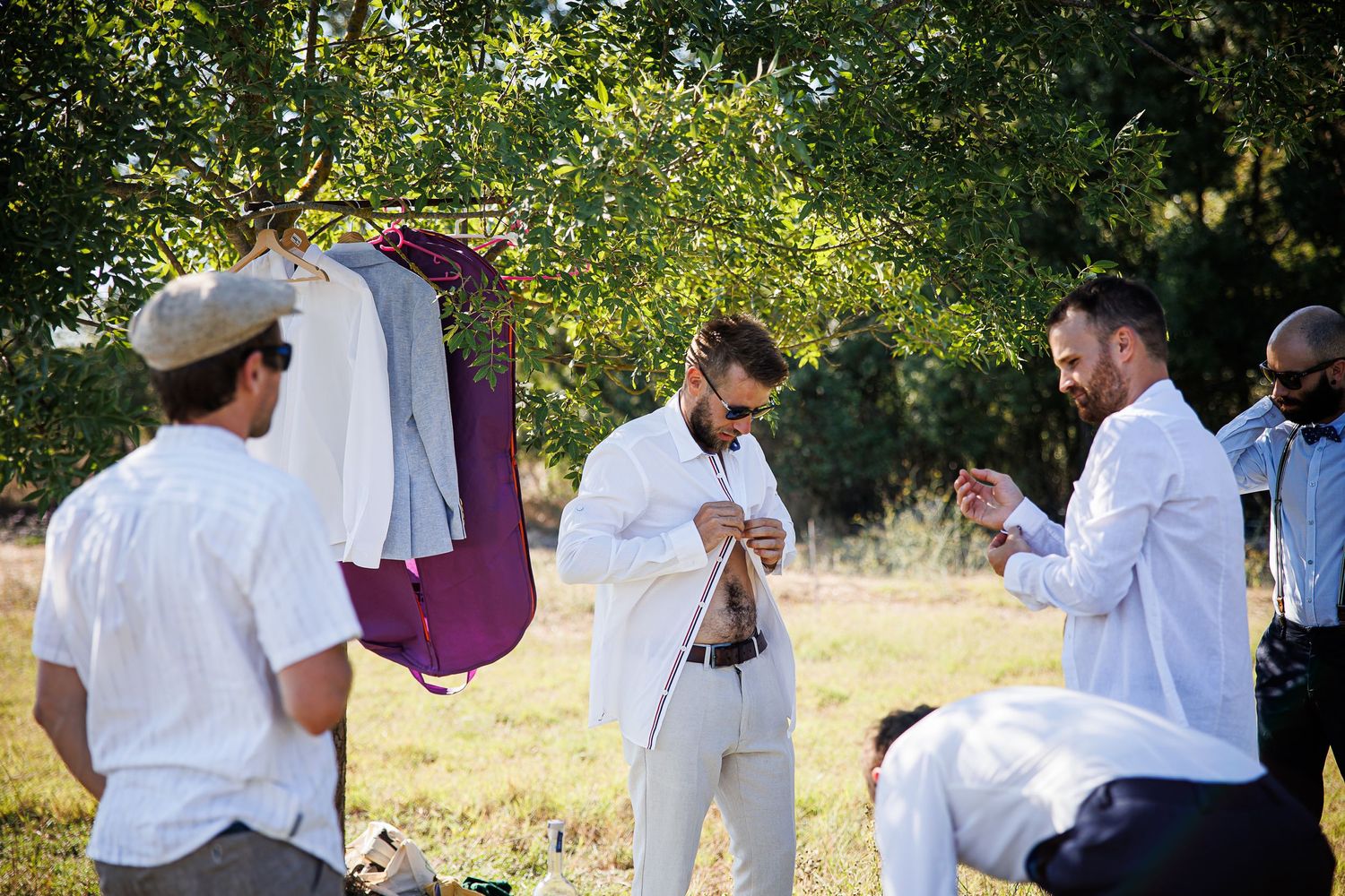 A group getting ready outdoors with formal white attire hanging on a portable rack.