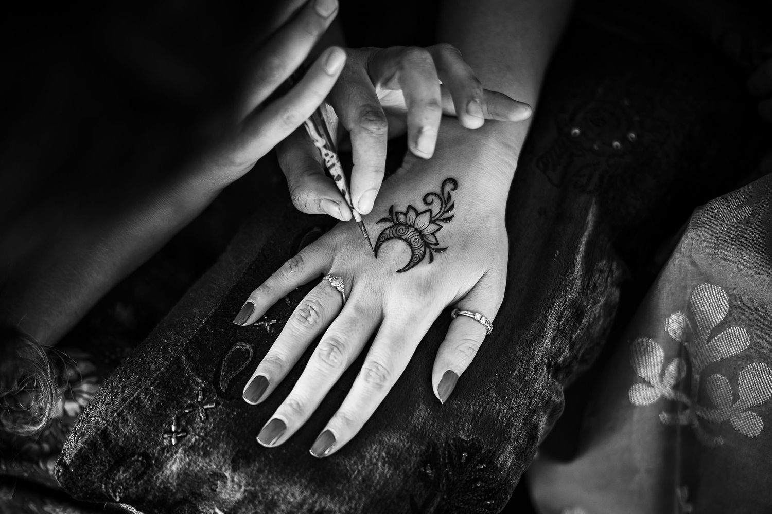 Close-up black and white photo of intricate henna design being applied to a hand.