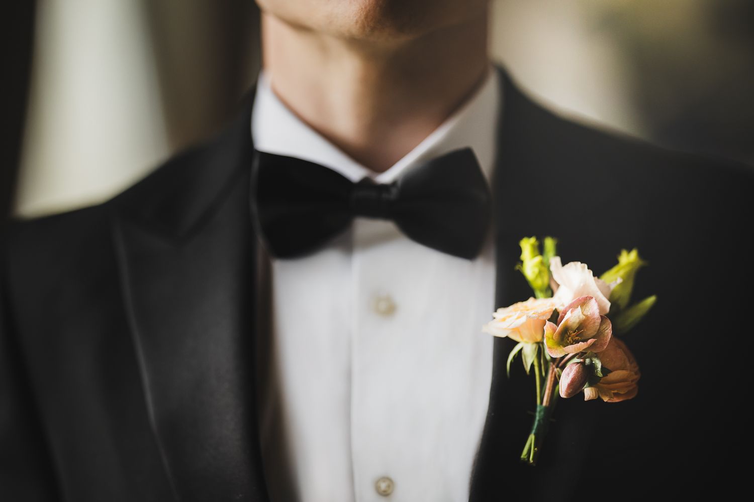 Close up of groom's boutonniere with pink and yellow flowers on black tuxedo lapel.