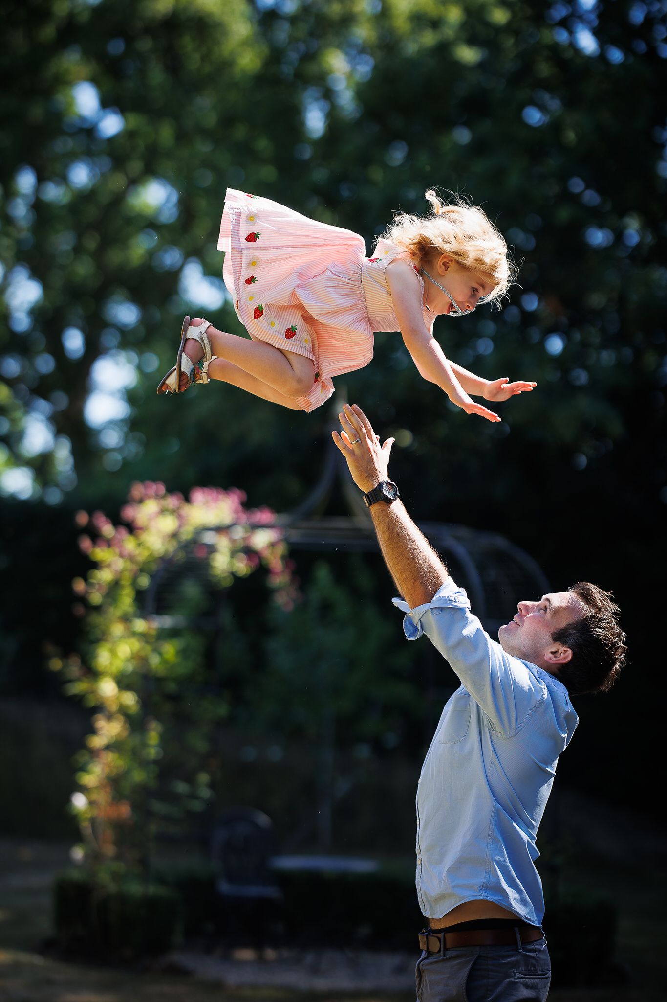 Joyful moment of a child being tossed in the air in a garden setting.