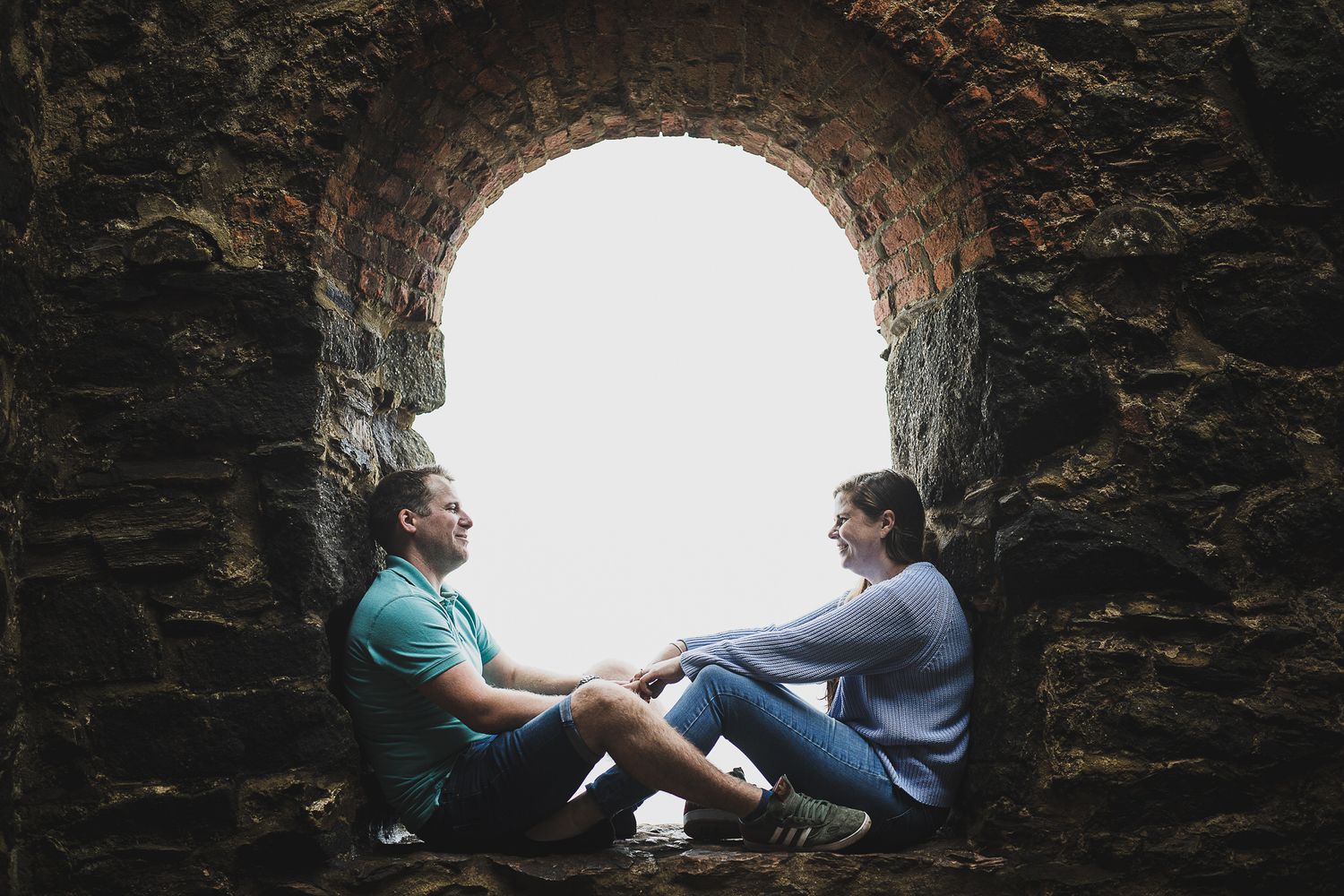 Two people sitting in a stone archway having an intimate conversation.